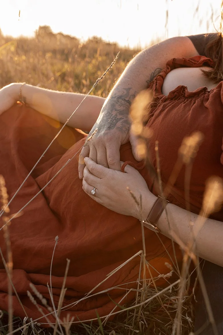 Intimate image of couples hands together on expectant mother's stomach at golden hour