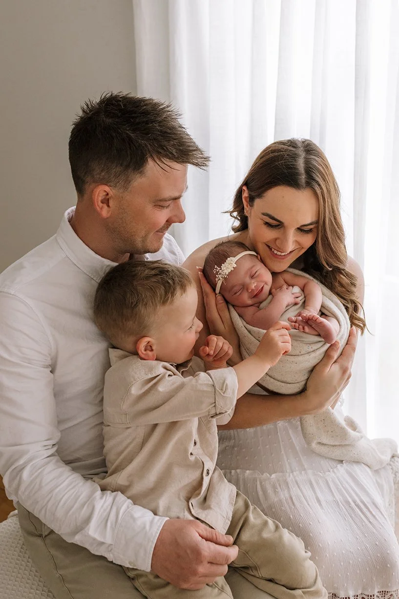 Newborn baby surrounded by their family in a studio portrait.
