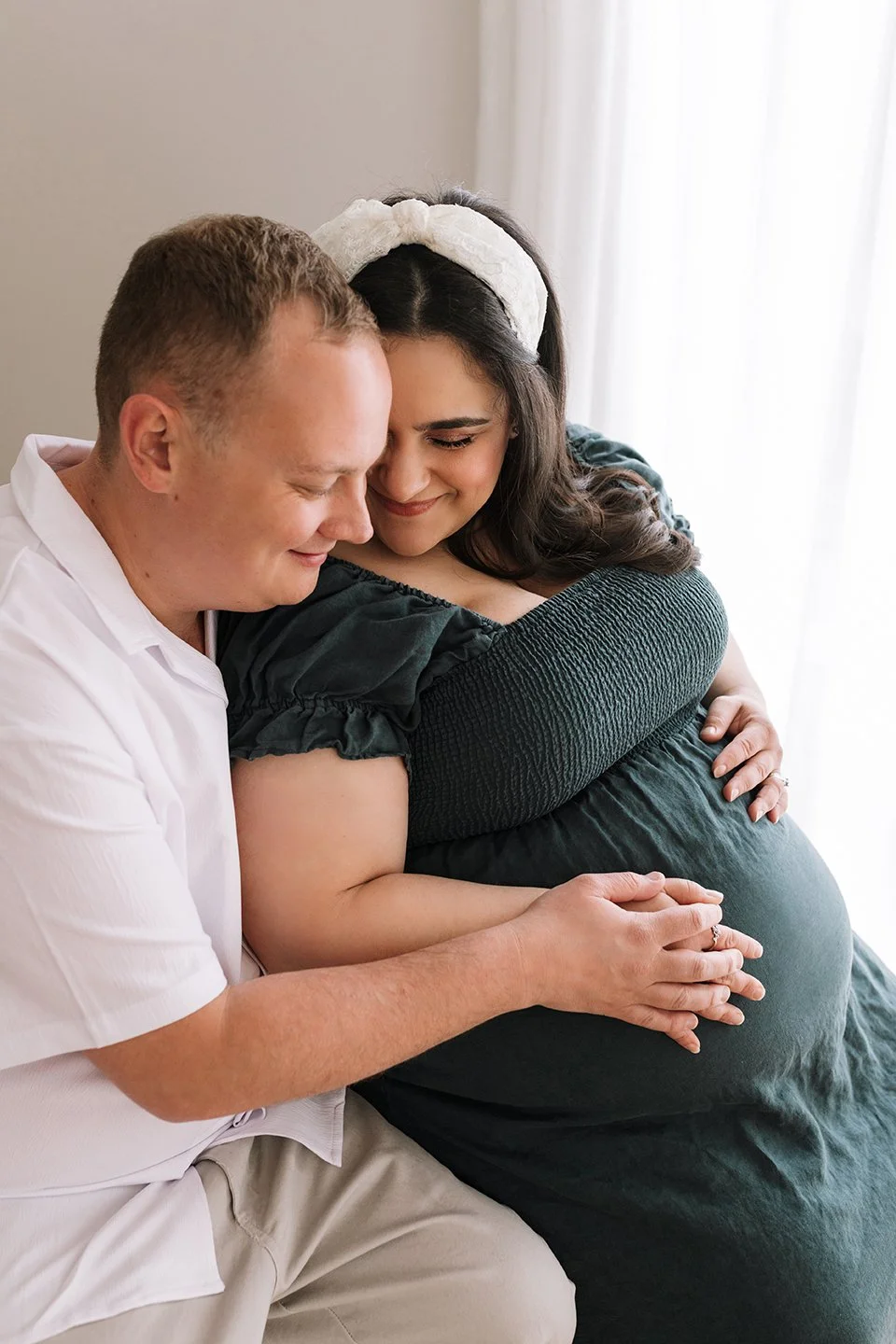 Future parents sharing a connected moment in natural light photography studio