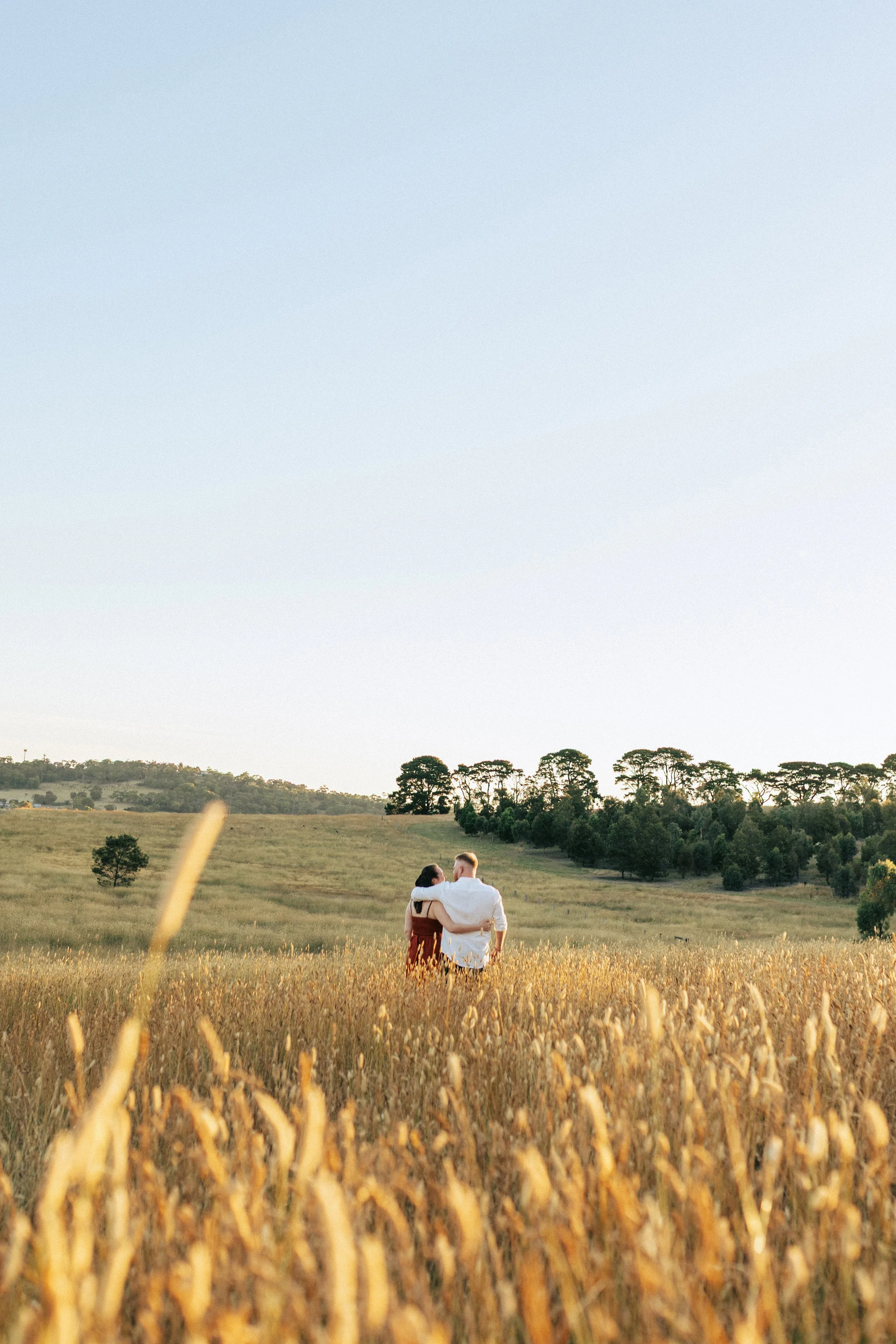 Couple embrace in open field at sunset