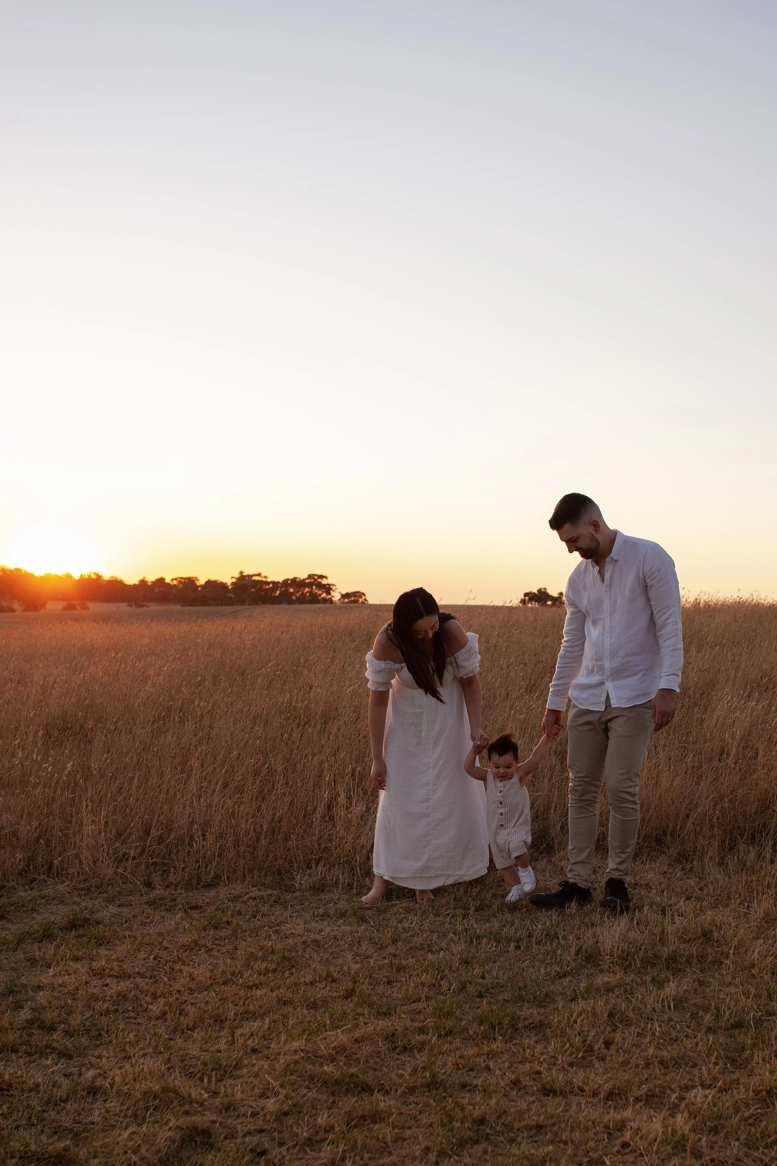Parents walking hand in hand with their child at sunset