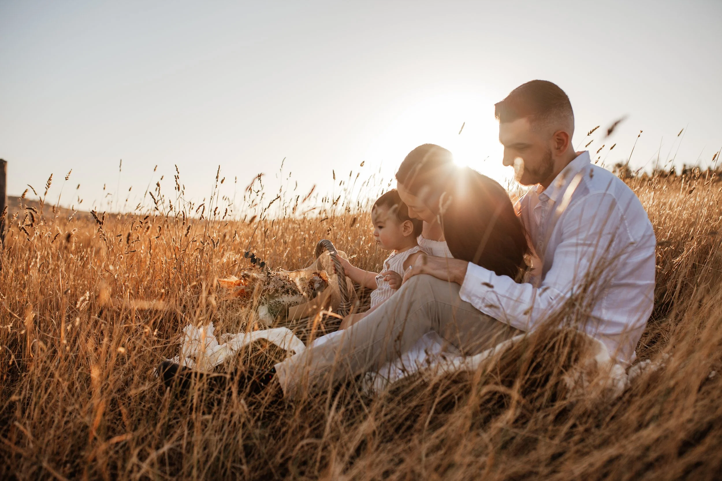 Parent sitting with their toddler in long grass at sunset
