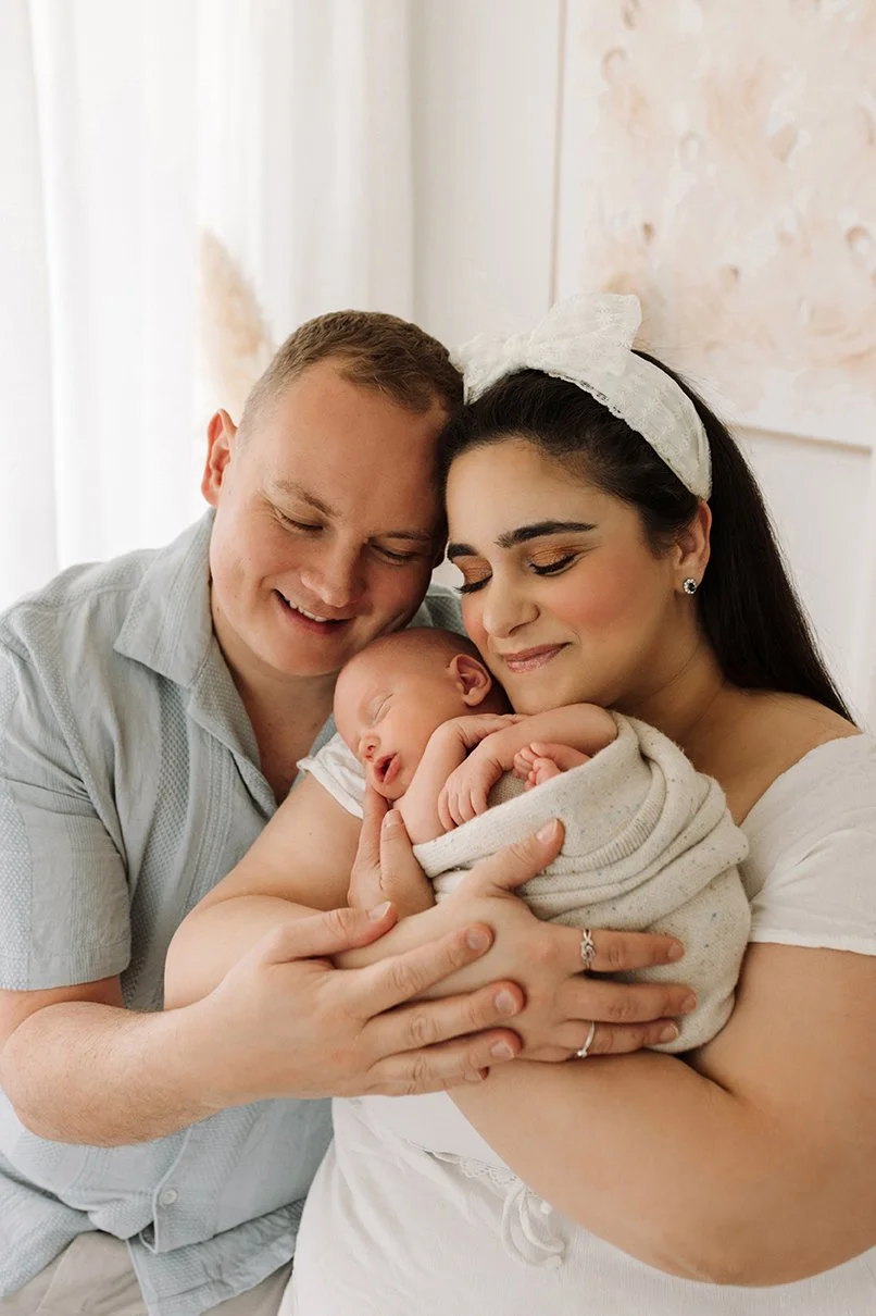 Parents cuddling their newborn baby during a natural studio session.