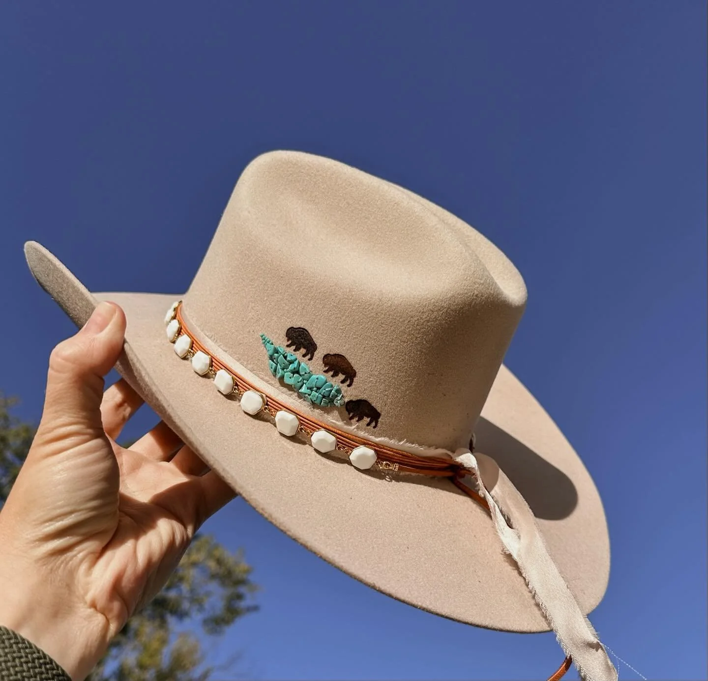 This Wyoming bride didn&rsquo;t walk down the aisle&hellip;
she rode in on a horse. 🐎

So obviously the hat had to match the energy.

Swipe &rarr;

A turquoise-beaded lake.
Three buffalo brands circling the water.
Her wedding date burned into the si