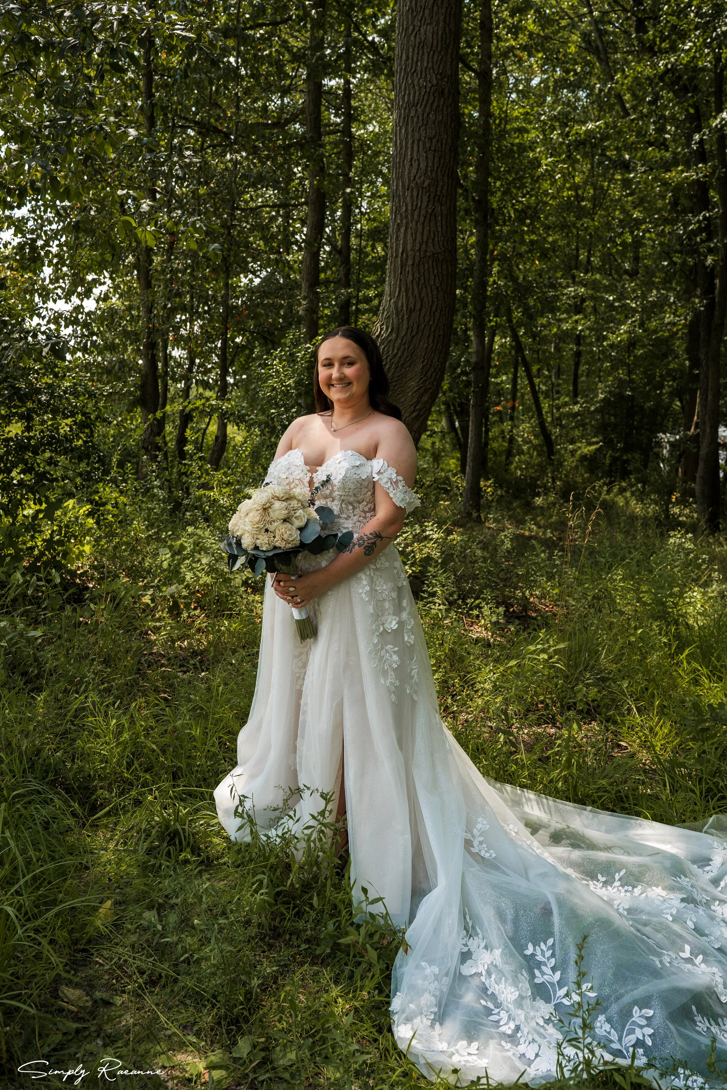A bride in a white wedding dress holding a bouquet of flowers in a green forest.