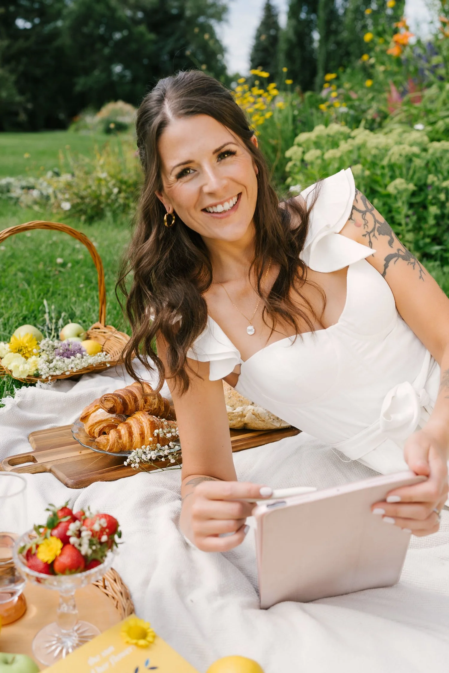 Bryony, CEO of Sunshine Pixel, smiling at camera while drawing logo design on her iPad in a sunny park, showcasing creativity and connection for entrepreneurs.