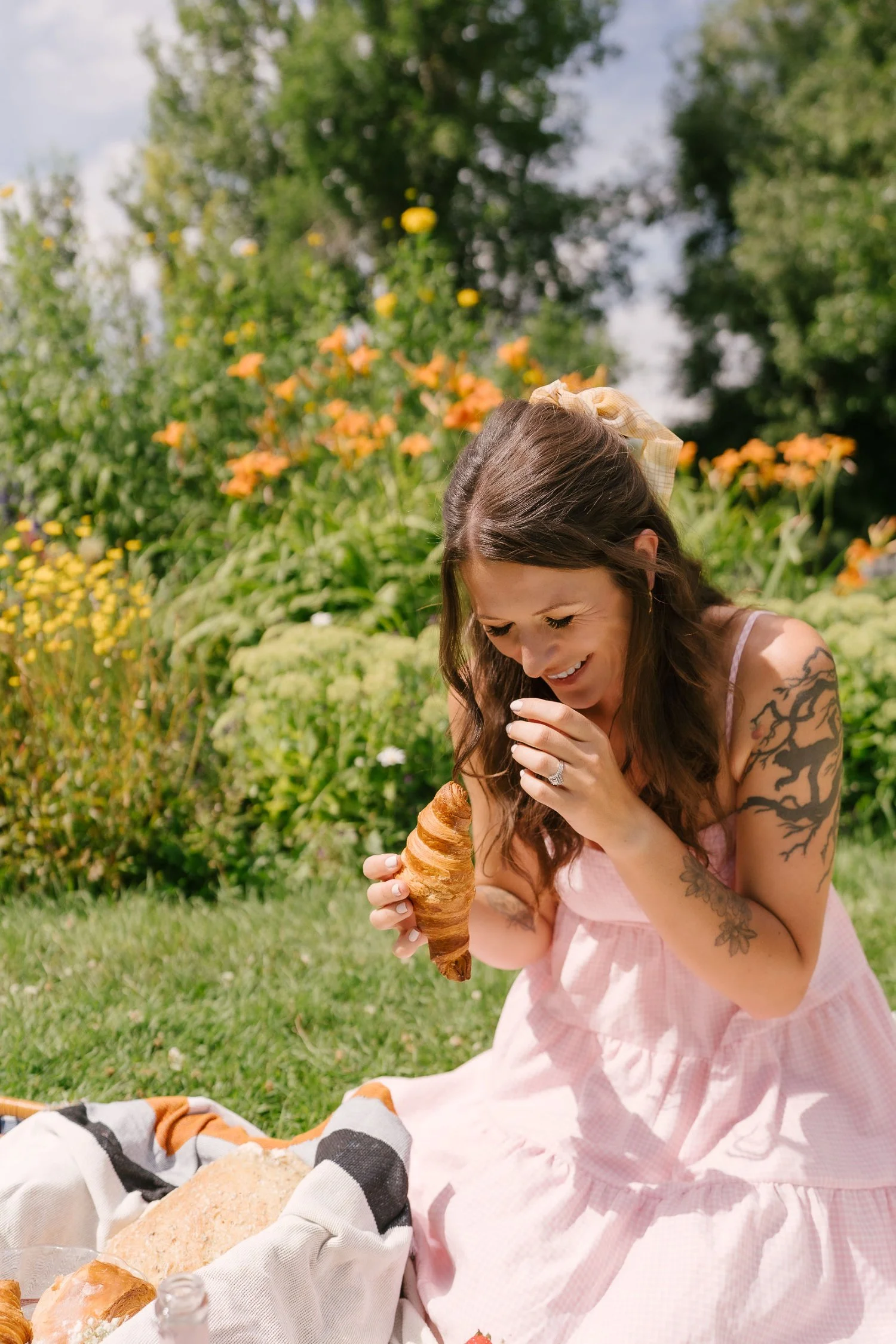 Bryony, a brand and web designer, smiling, enjoying a picnic with a croissant on a sunny day, embodying relaxed and approachable brand vibes.