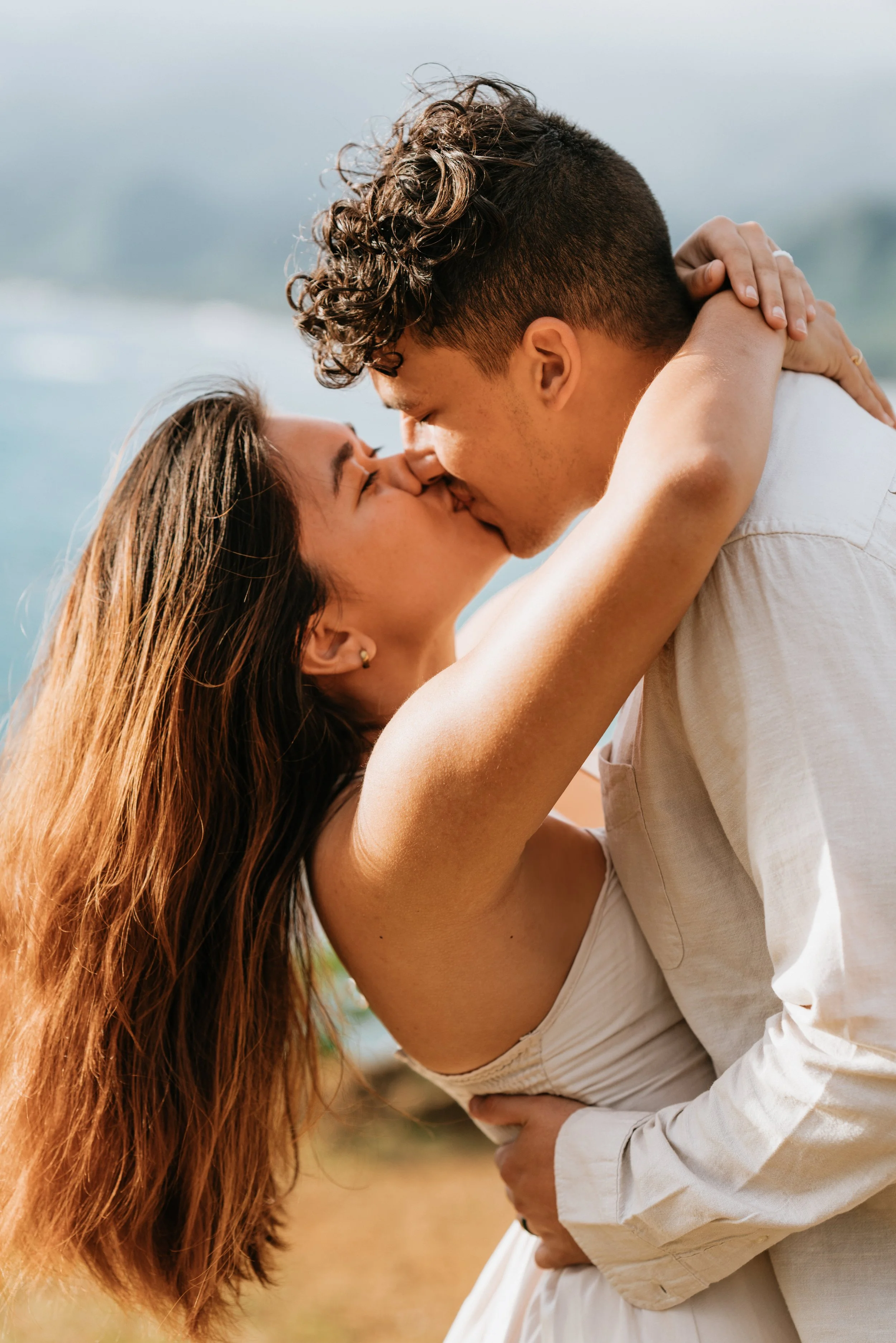 A couple kissing outdoors with the ocean in the background