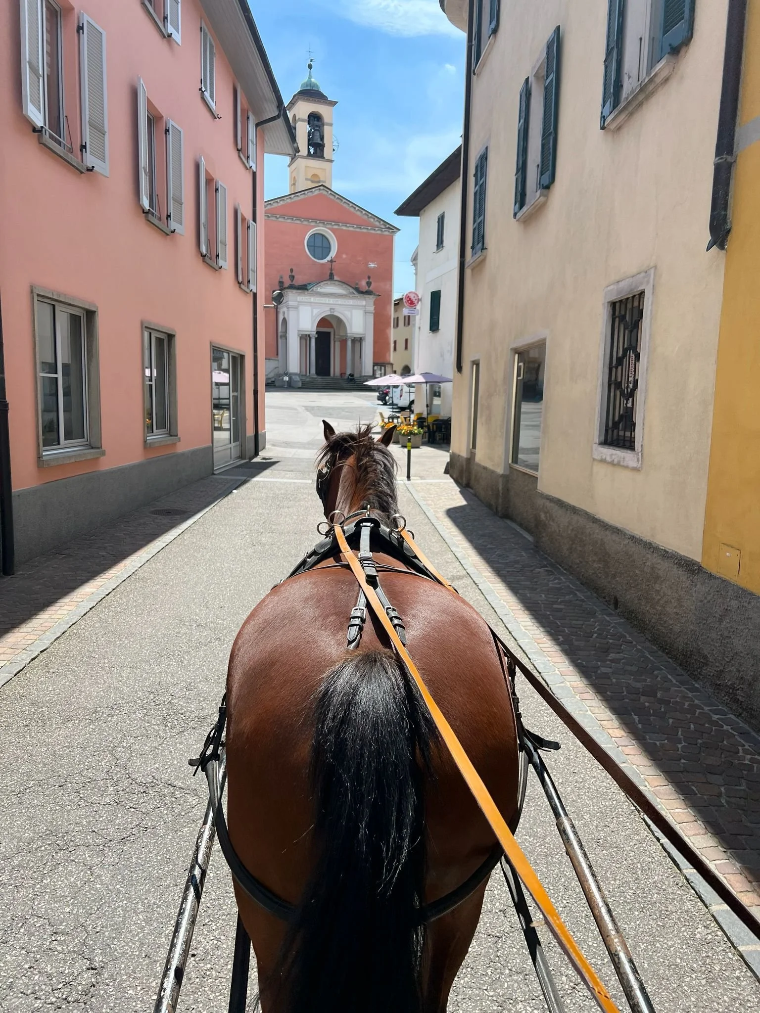 Rumore degli zoccoli di un cavallo in una strada stretta tra edifici colorati di Stabio, con la Chiesa dei Santi Giacomo e Cristoforo
