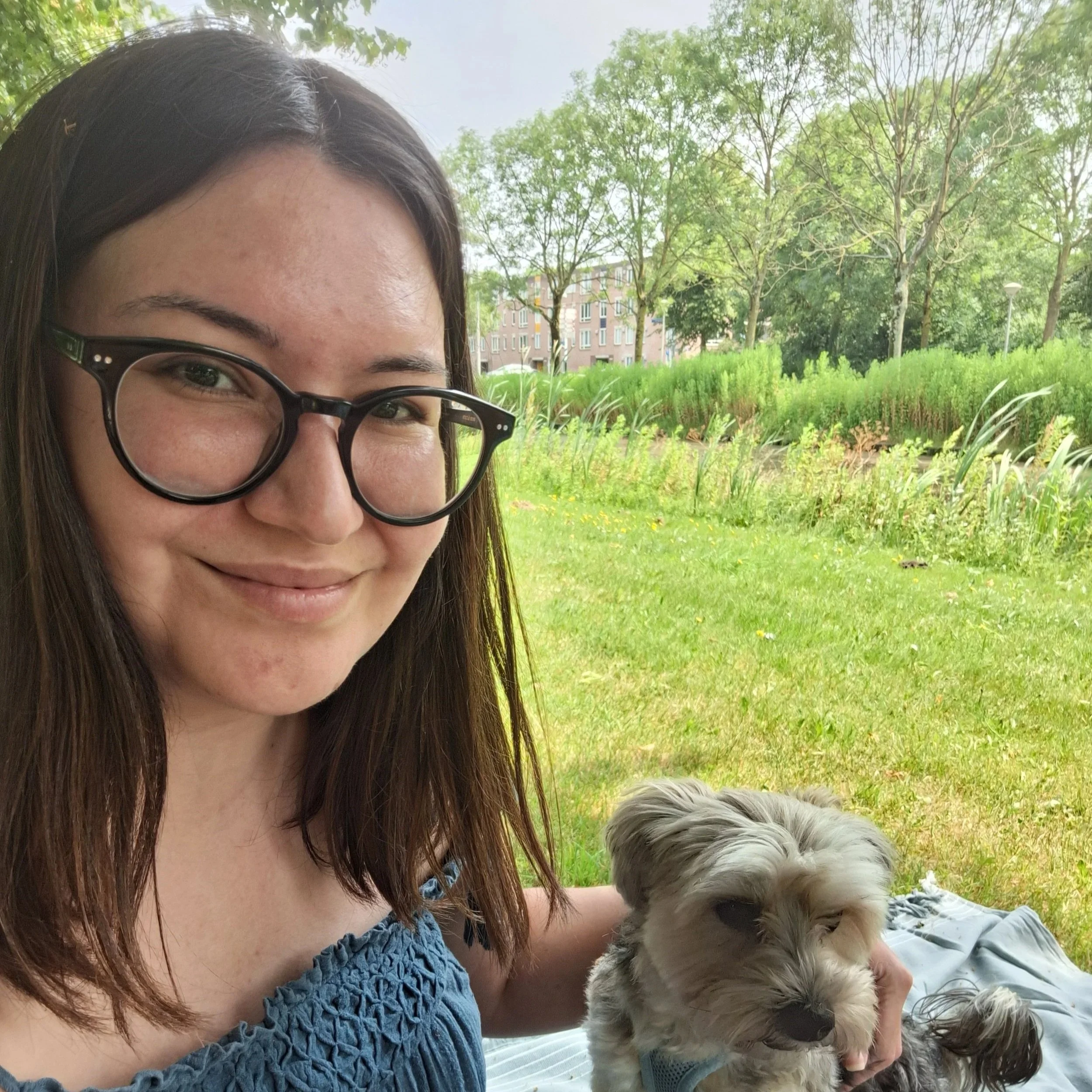 A young woman with glasses and long dark hair holding a beagle puppy outdoors on a tree-lined sidewalk.