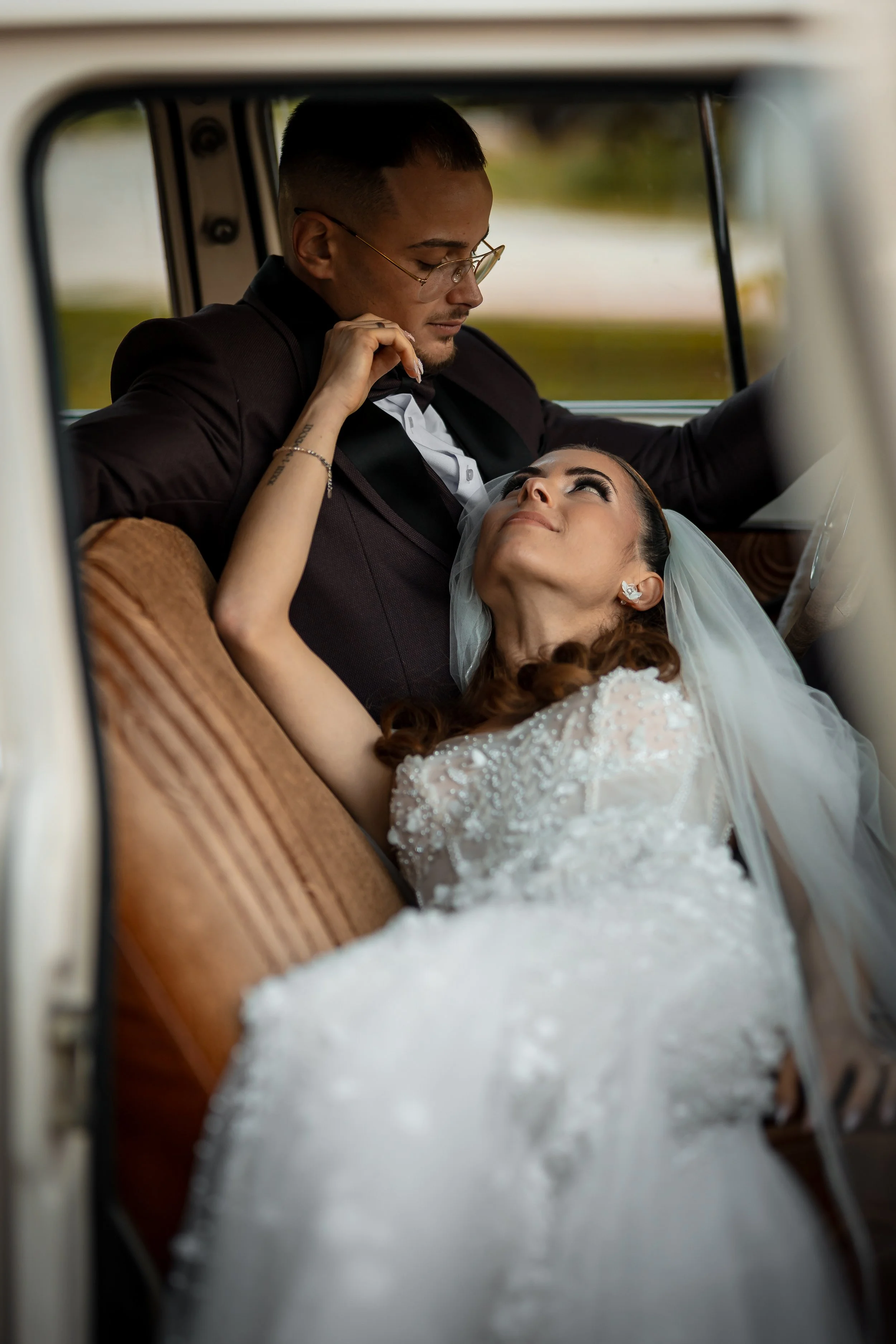 Bride and groom sitting closely in a vintage car, gazing at each other.