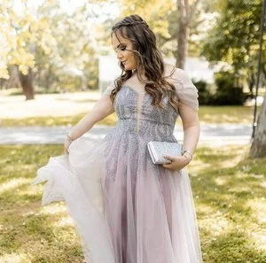 Woman in a flowing pastel-colored dress holding a clutch in a park.