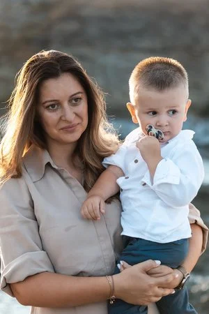 Woman holding a young boy outdoors, with the woman looking content and the boy sucking on a pacifier.