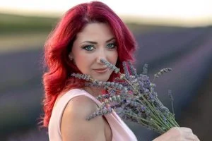 A woman with pink hair holding a bouquet of lavender flowers outdoors.