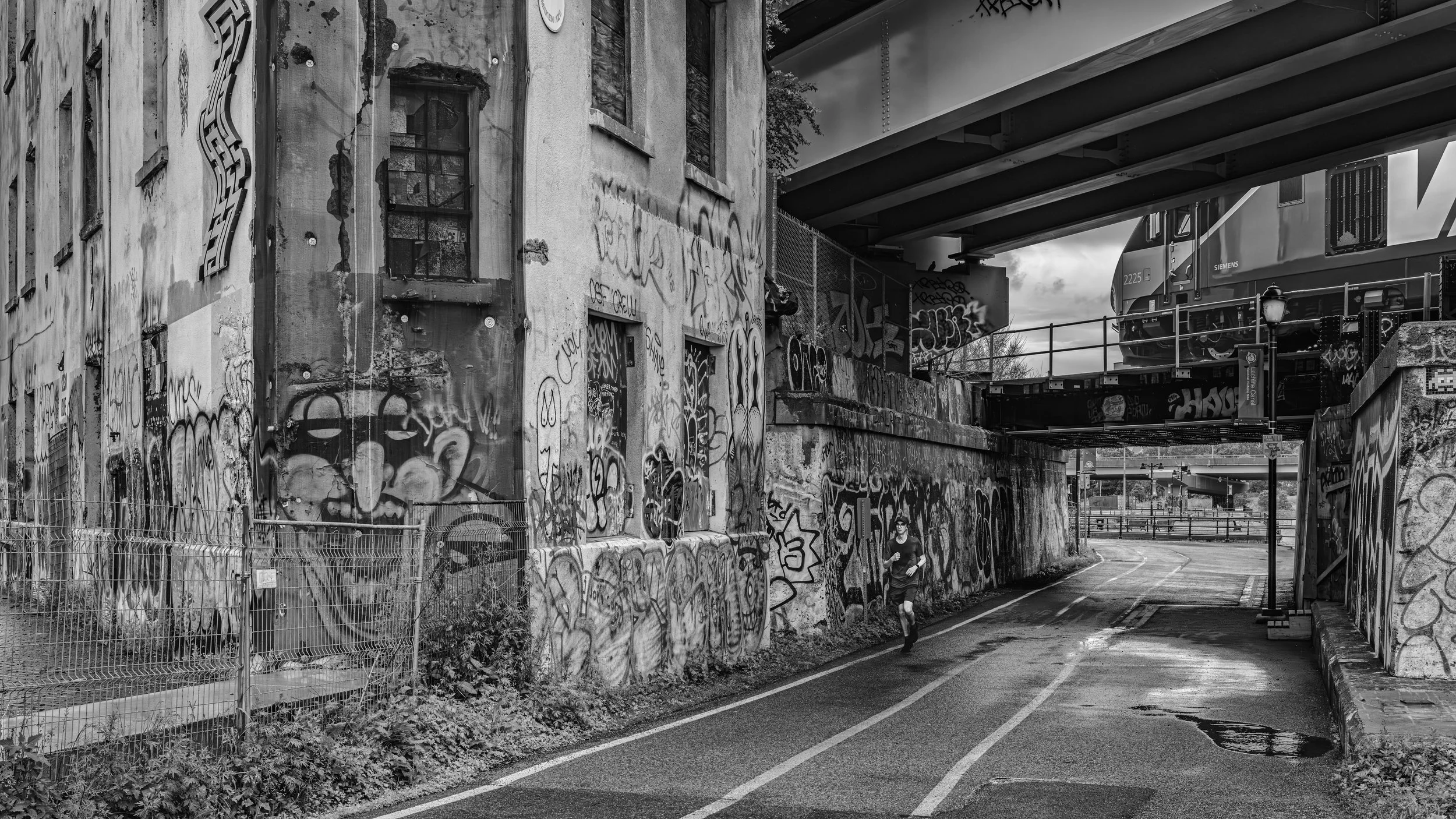 A woman jogging under a bridge over a graffiti-covered wall next to a street.
