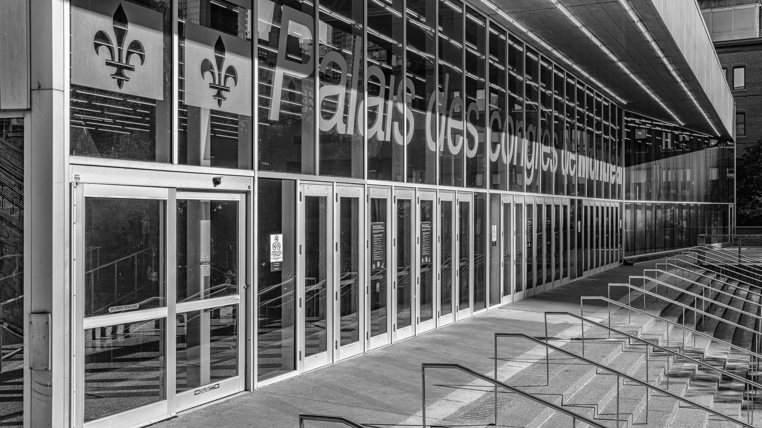 Exterior view of a modern glass building with large signage in French, featuring an entrance with glass doors and a staircase with metal railings outside.