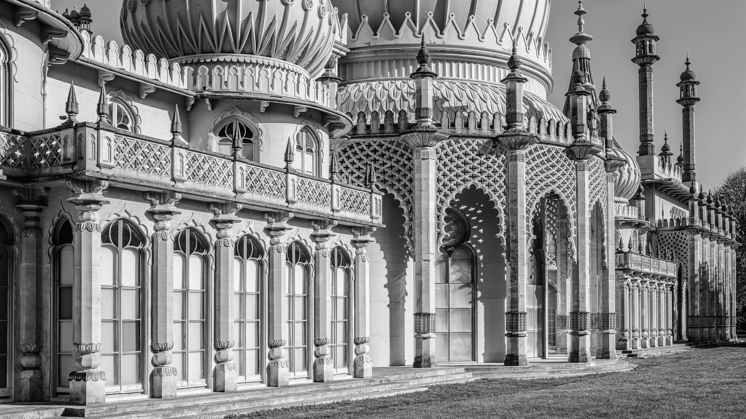 Close-up of an ornate, historic building with detailed architectural features, arched windows, decorative railings, and spires in black and white.