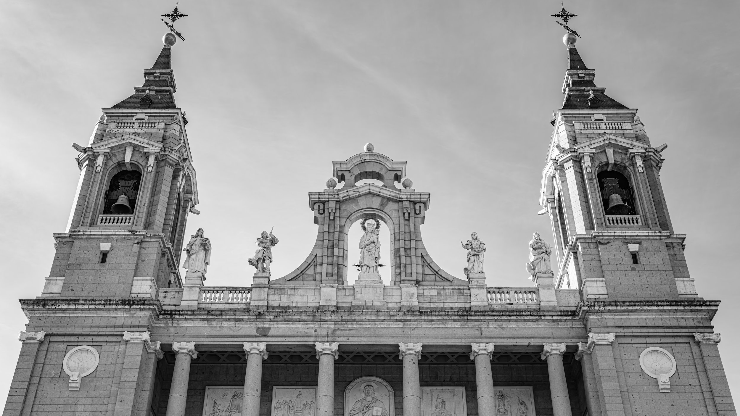 Black and white photograph of a church facade with two tall bell towers and religious statues at the top.