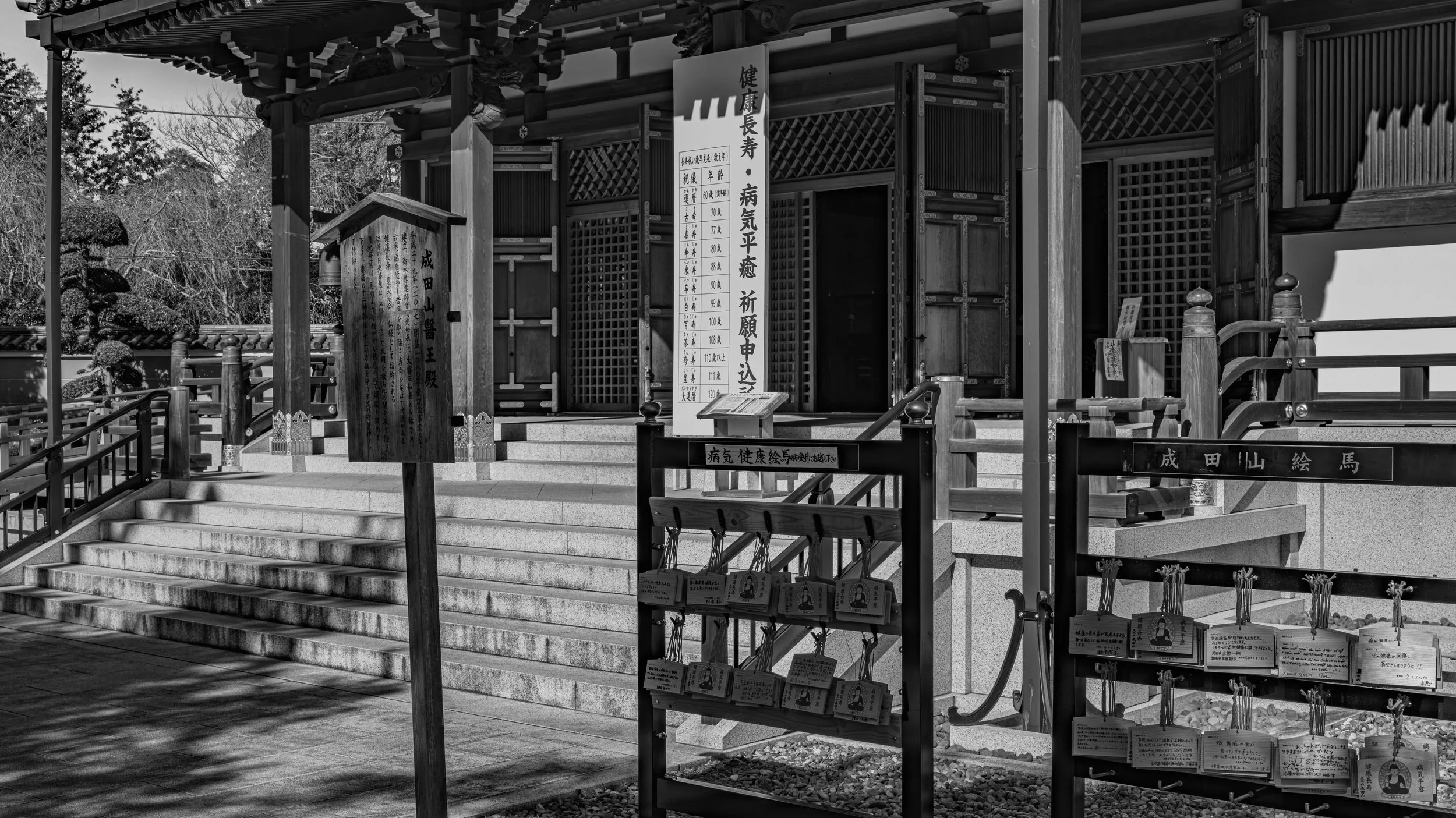 A traditional Japanese shrine with steps leading up to the entrance, featuring wooden structures and signs with Japanese writing.