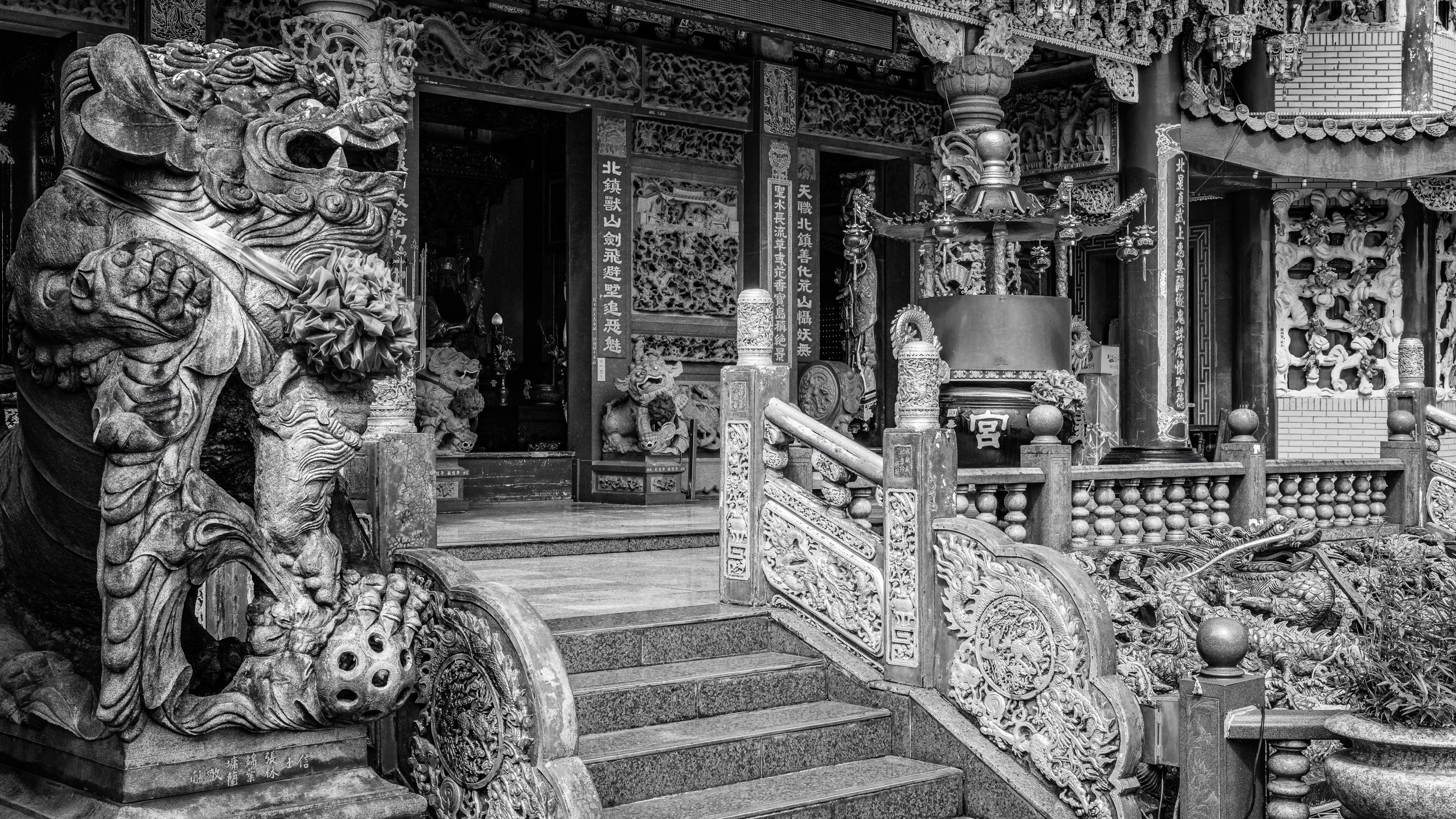 Black and white photo of a traditional Asian temple entrance with ornate carvings, dragon statues, and decorative lanterns.