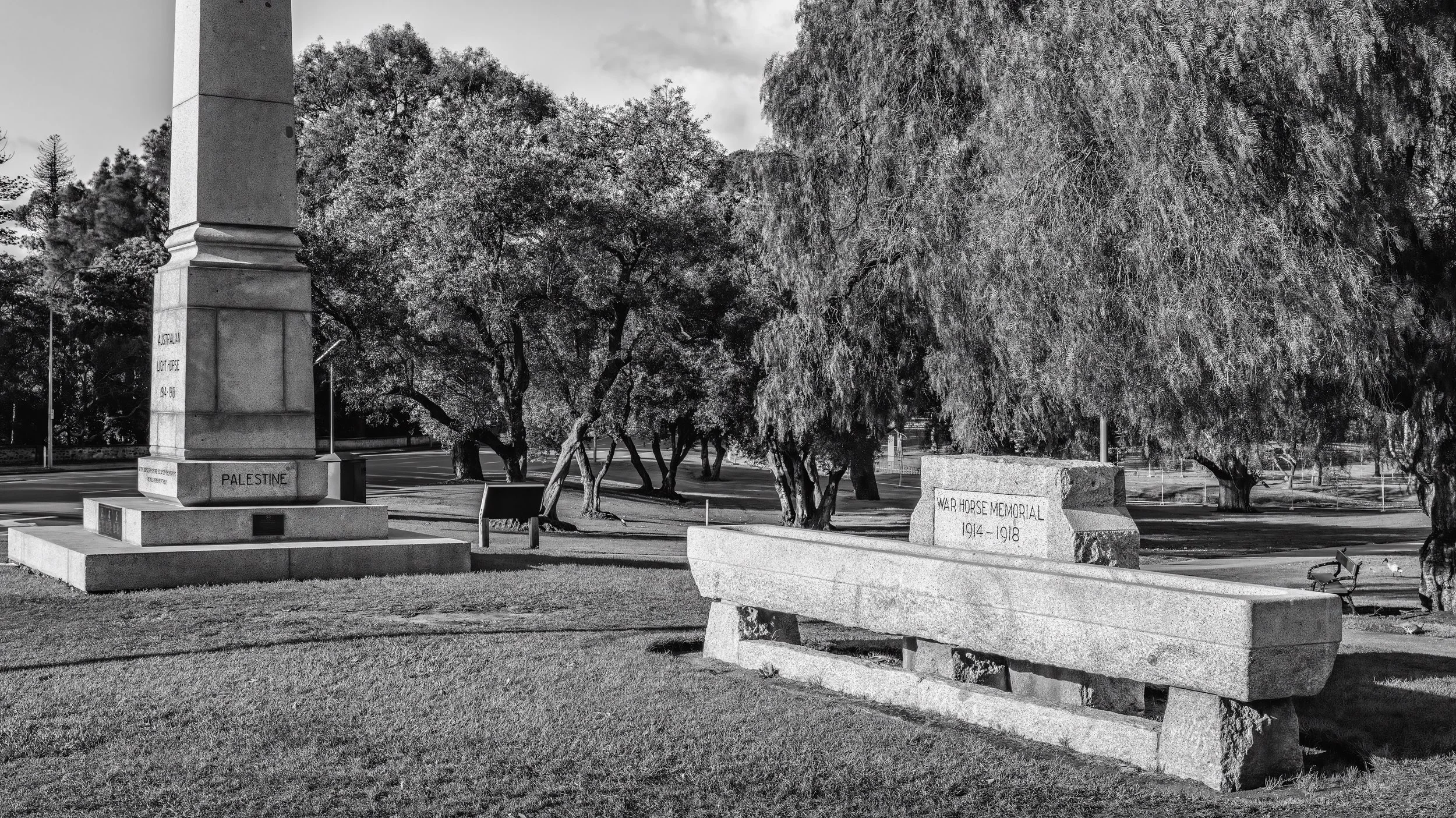 Black and white photo of memorials and a park with trees visible in the background. Adelaide, Australia.
