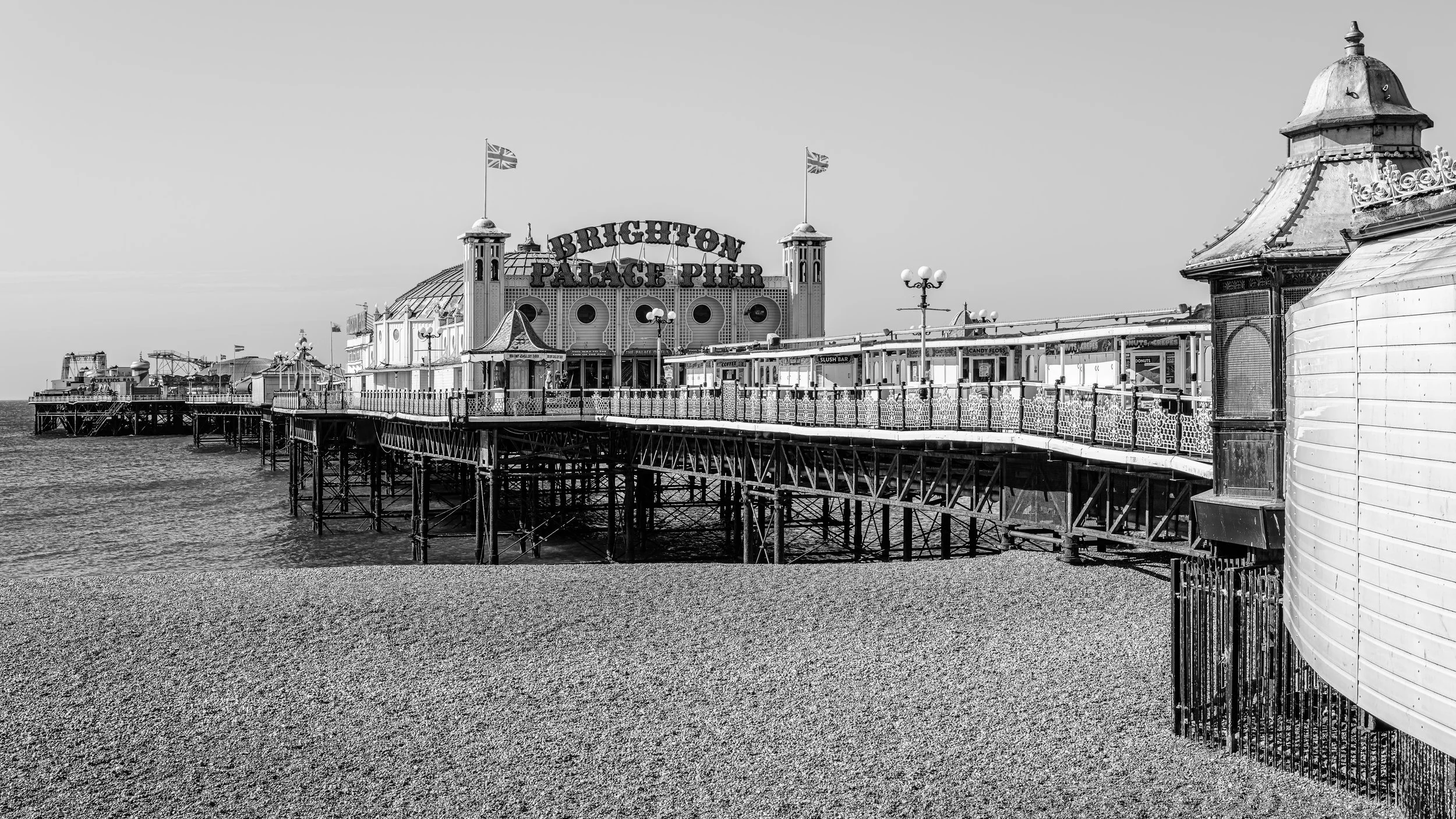 Black and white photo of Brighton Palace Pier with amusement rides and seaside shops extending into the ocean.