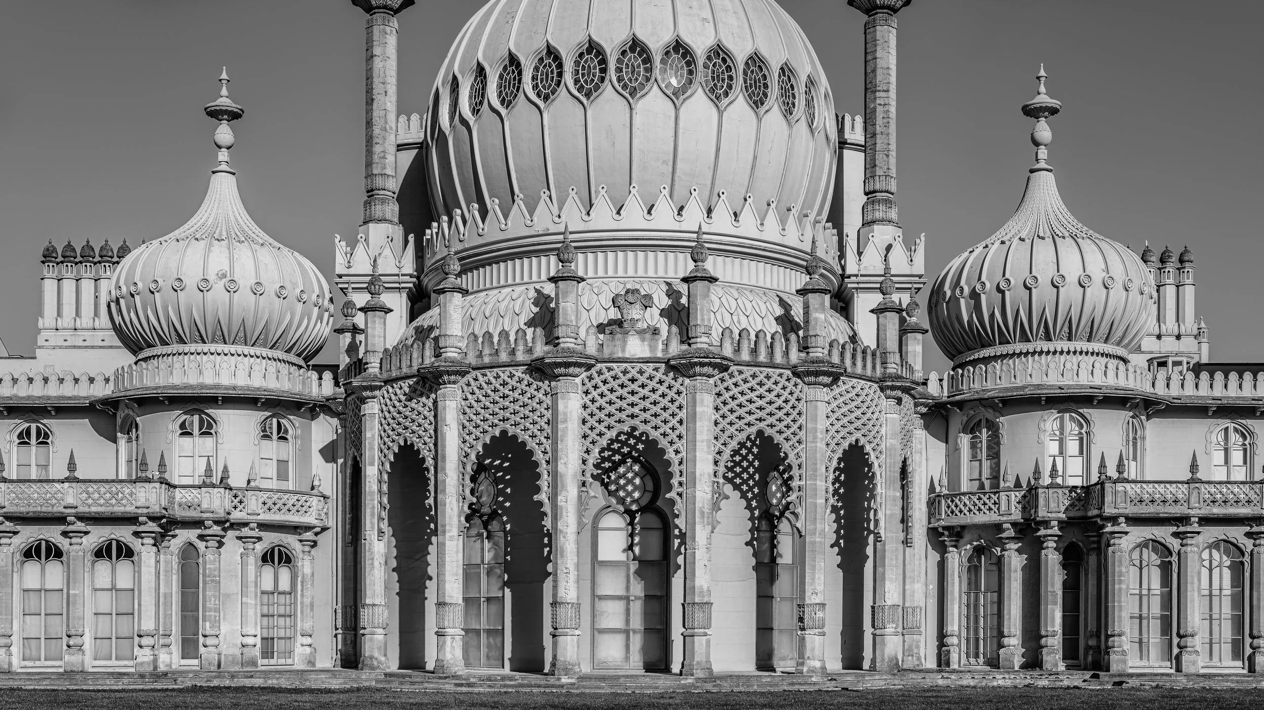 Black and white photo of a grand Islamic palace with ornate domes and minarets, featuring intricate lattice work, arched windows, and decorative details.