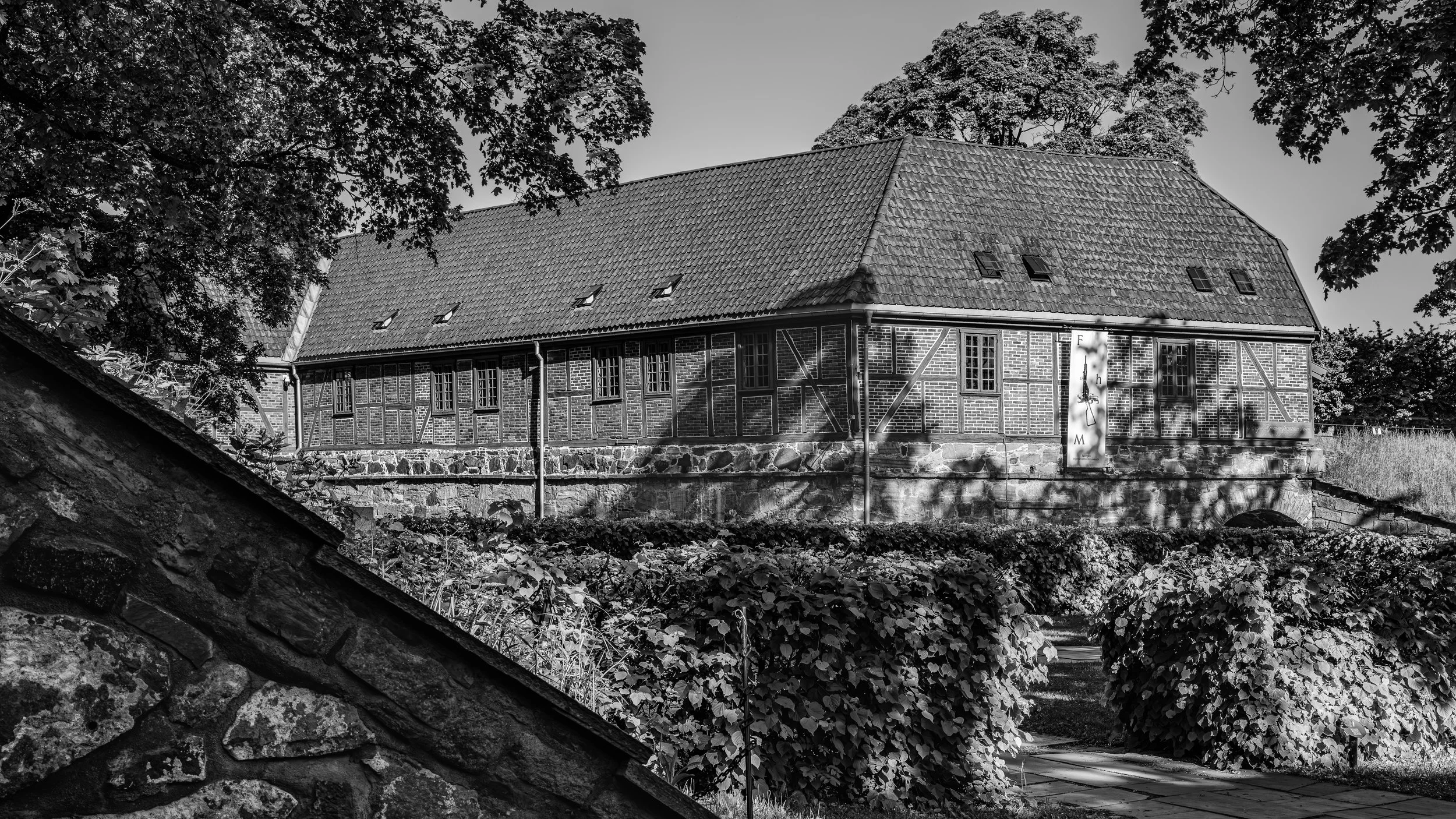 Black and white photo of a large house with a tiled roof, surrounded by trees and foliage.