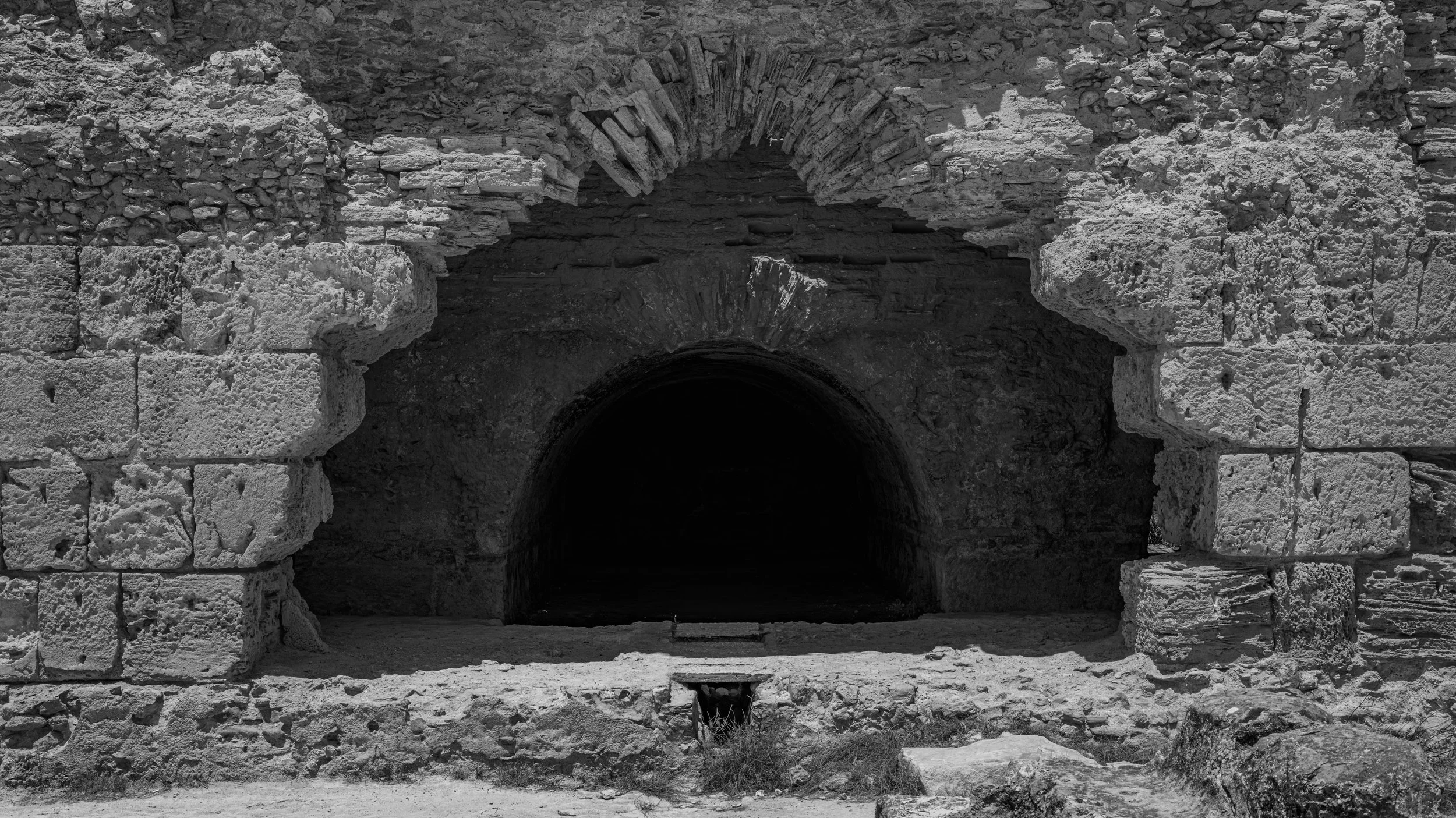 Ancient stone archway with brickwork inside a historic stone structure, in black and white.