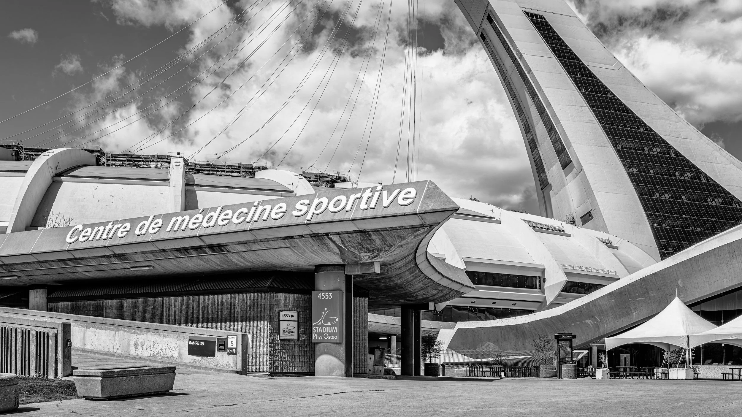 The exterior of a modern sports medicine center with a sign that reads 'Centre de médecine sportive' and a large, distinctive building in the background, partially visible through a partly cloudy sky.