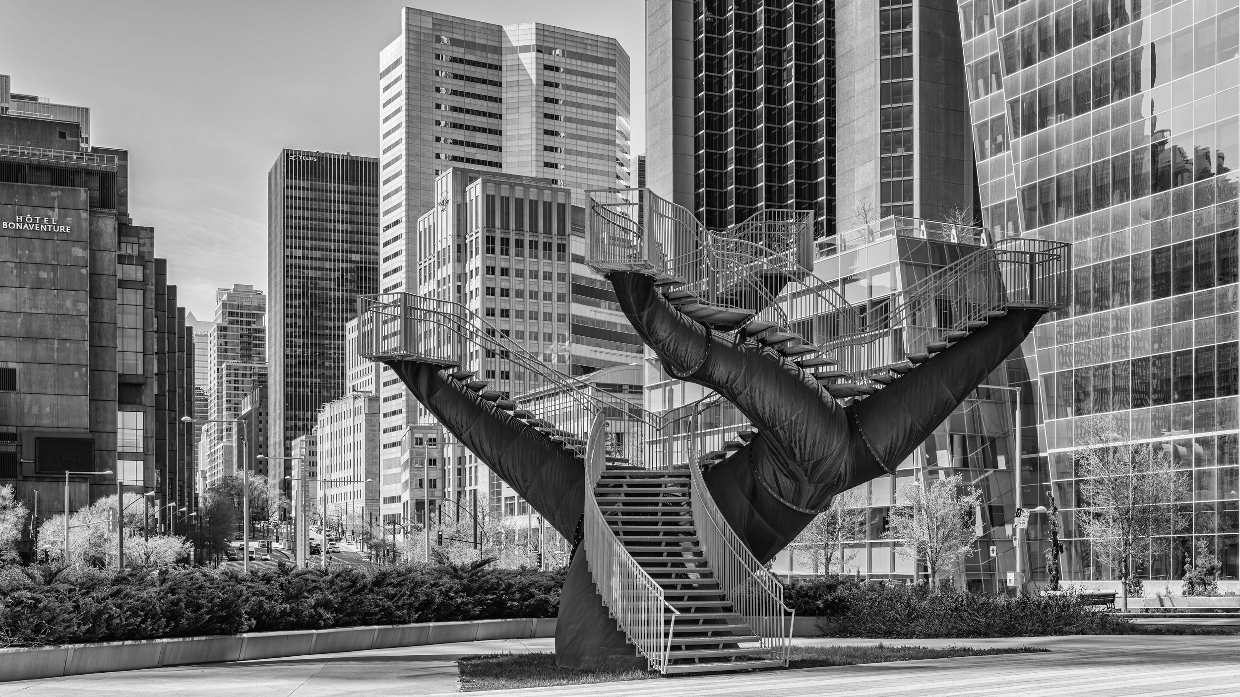 A large sculpture of a hand with an open palm and extended fingers, integrated with an industrial staircase, set against a backdrop of modern skyscrapers in an urban cityscape.