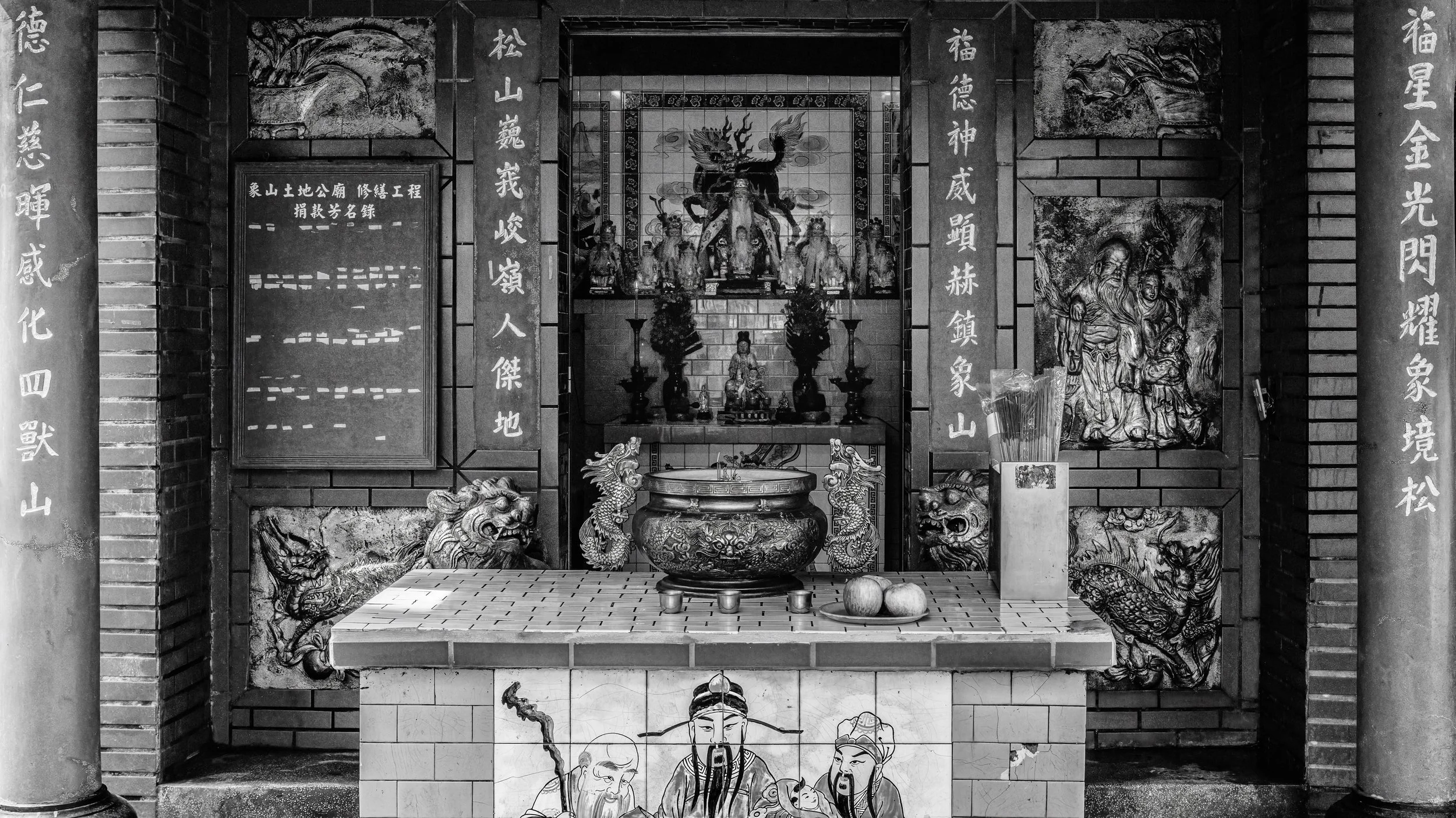 Black and white photo of a traditional Chinese shrine with statues, dragons, and calligraphy on the walls.