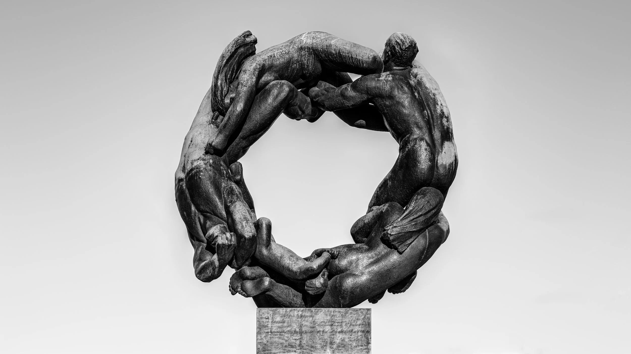 Black and white sculpture of two hands holding a figure of a person, forming a circular shape.