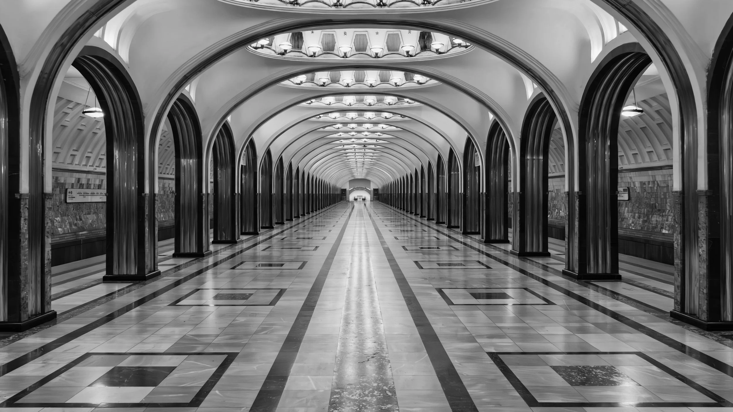 Empty underground metro station with arched ceilings, polished tiled floor, symmetrical lighting fixtures, and dark trim around the arches in black and white. Metro, Moscow, Russia.