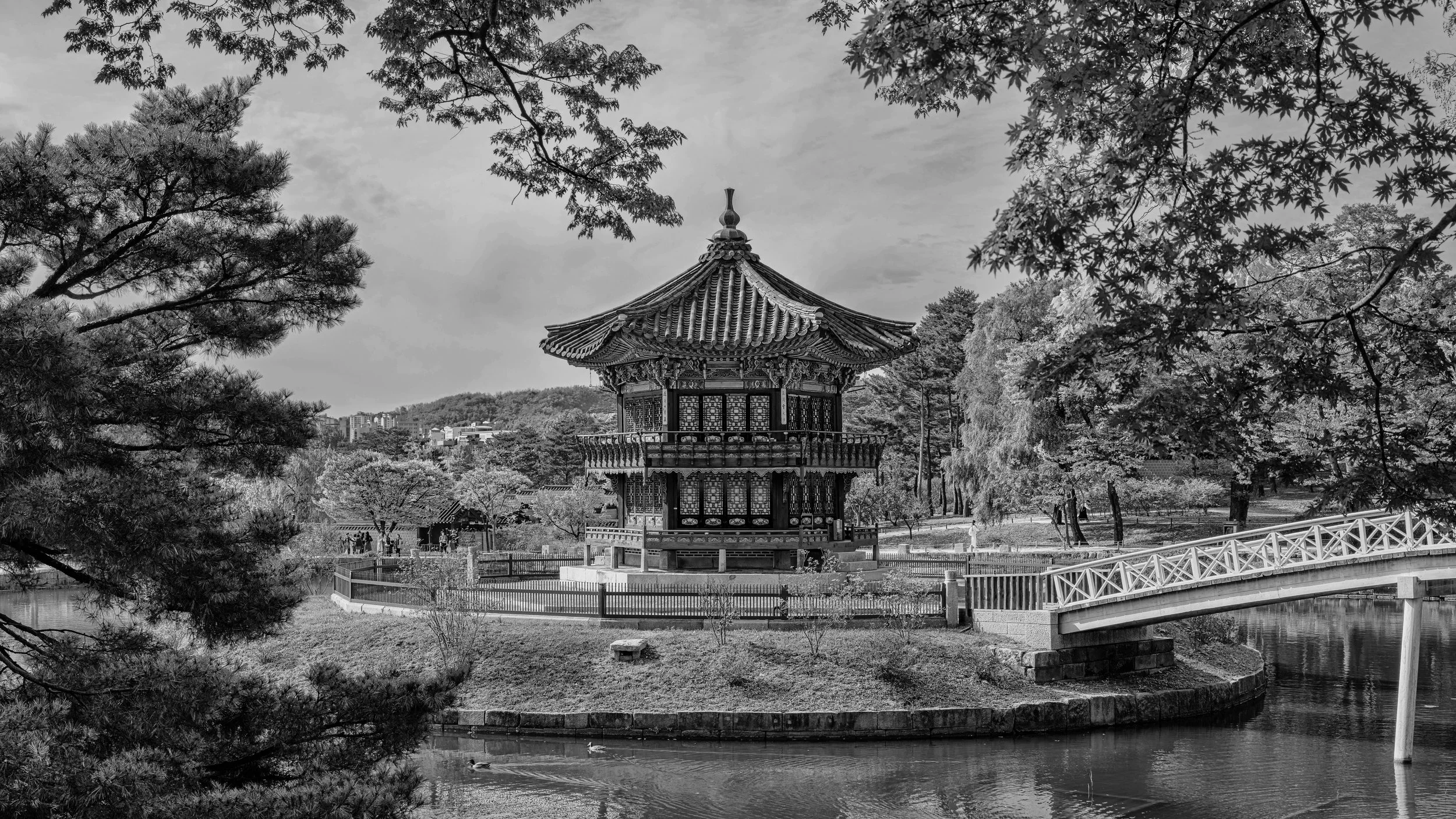 A traditional Asian pagoda-style pavilion in a park with trees, a small pond, and a bridge in black and white. Seoul, Korea.