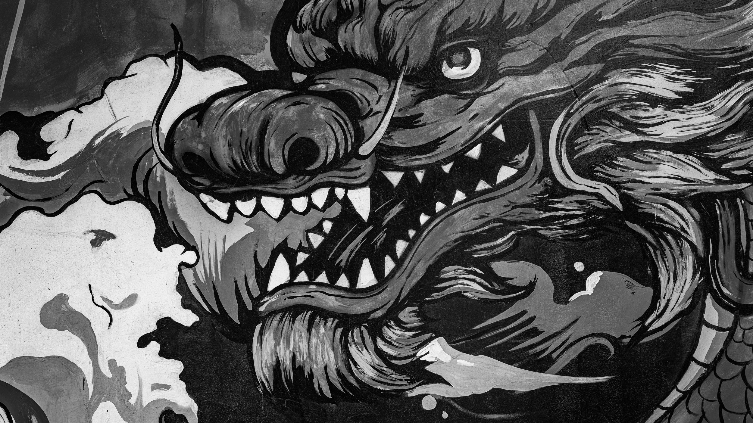 Black and white mural of a fierce dragon with sharp teeth, large eyes, and flowing mane on a textured wall.