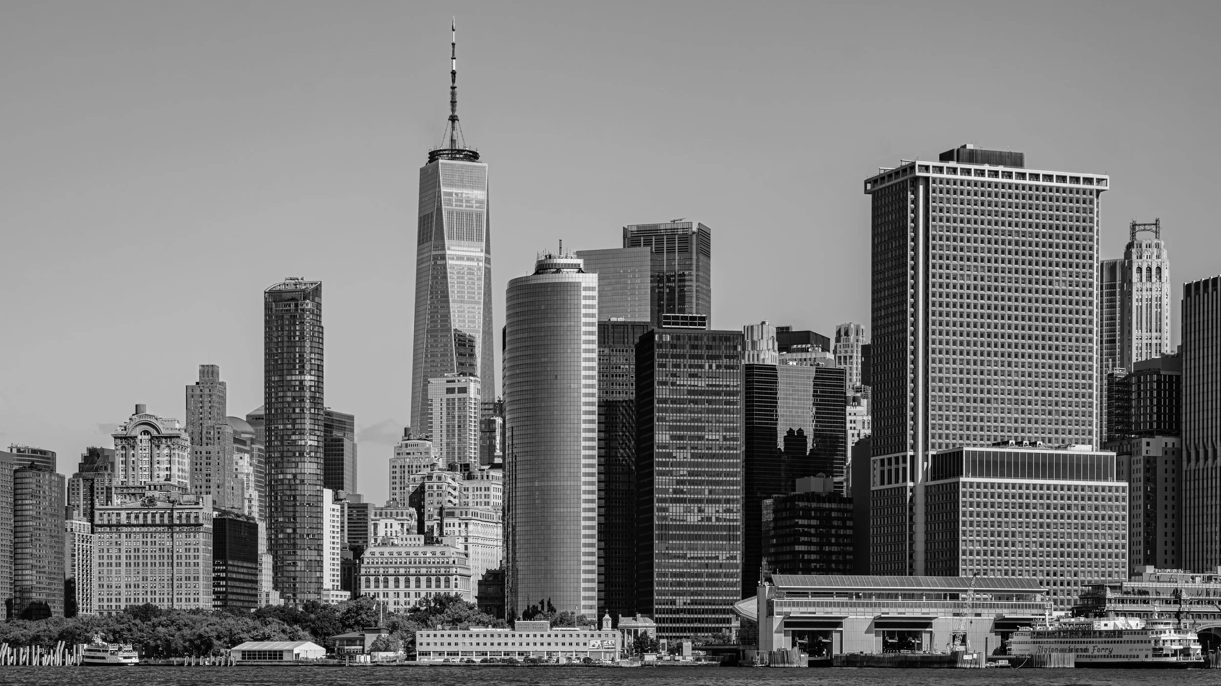 Black and white image of a city skyline featuring tall skyscrapers, including One World Trade Center, with a body of water in the foreground. Manhattan, New York, USA.
