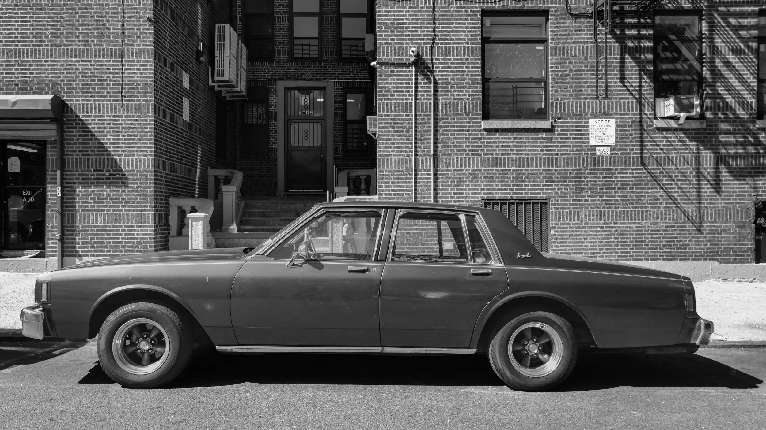 A vintage black car parked on the street in front of a brick building with stairs leading up to a door. The Bronxn, New York, USA.