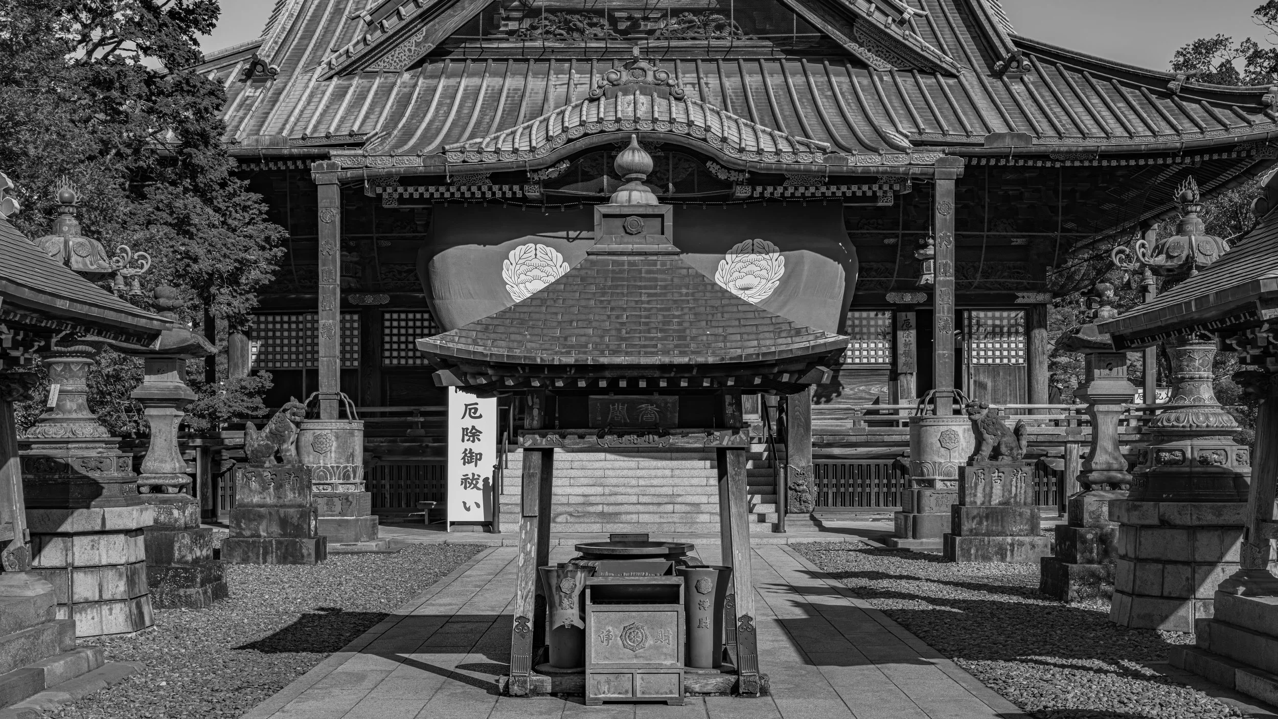 Traditional Japanese shrine with a roof, lanterns, and statues, black and white photo.