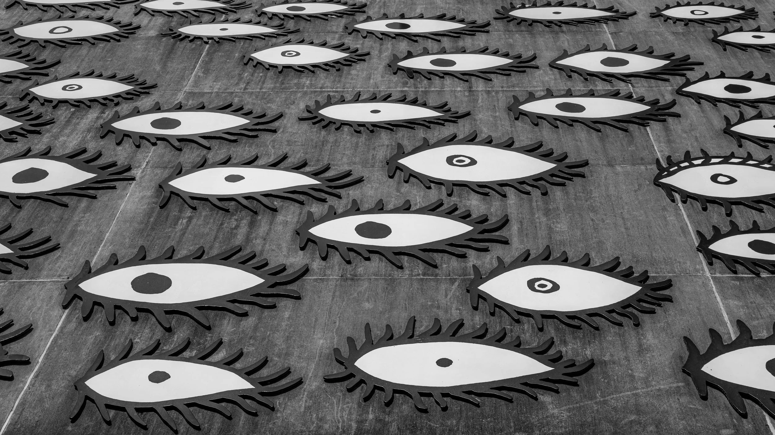 Multiple eye-shaped cutouts with black eyelashes and a dark iris, arranged on a tiled floor in a pattern.