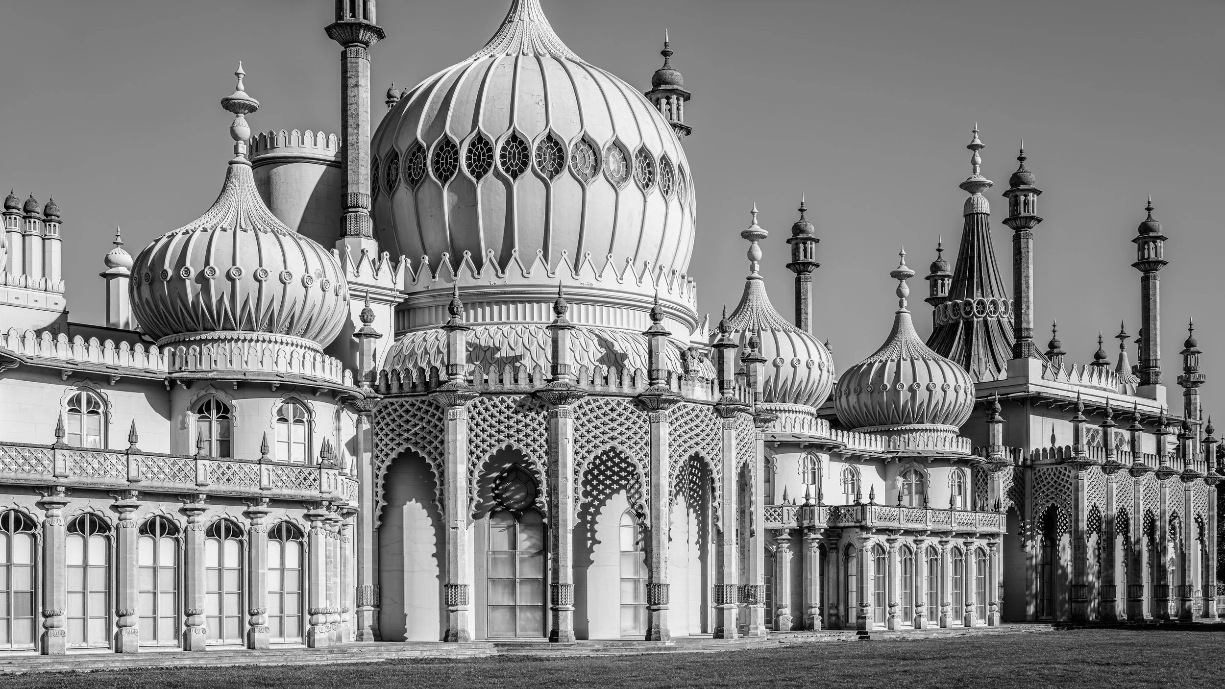 Black and white photograph of the ornate architecture of the Taj Mahal, showcasing its prominent domes, minarets, detailed carvings, and decorative arches.