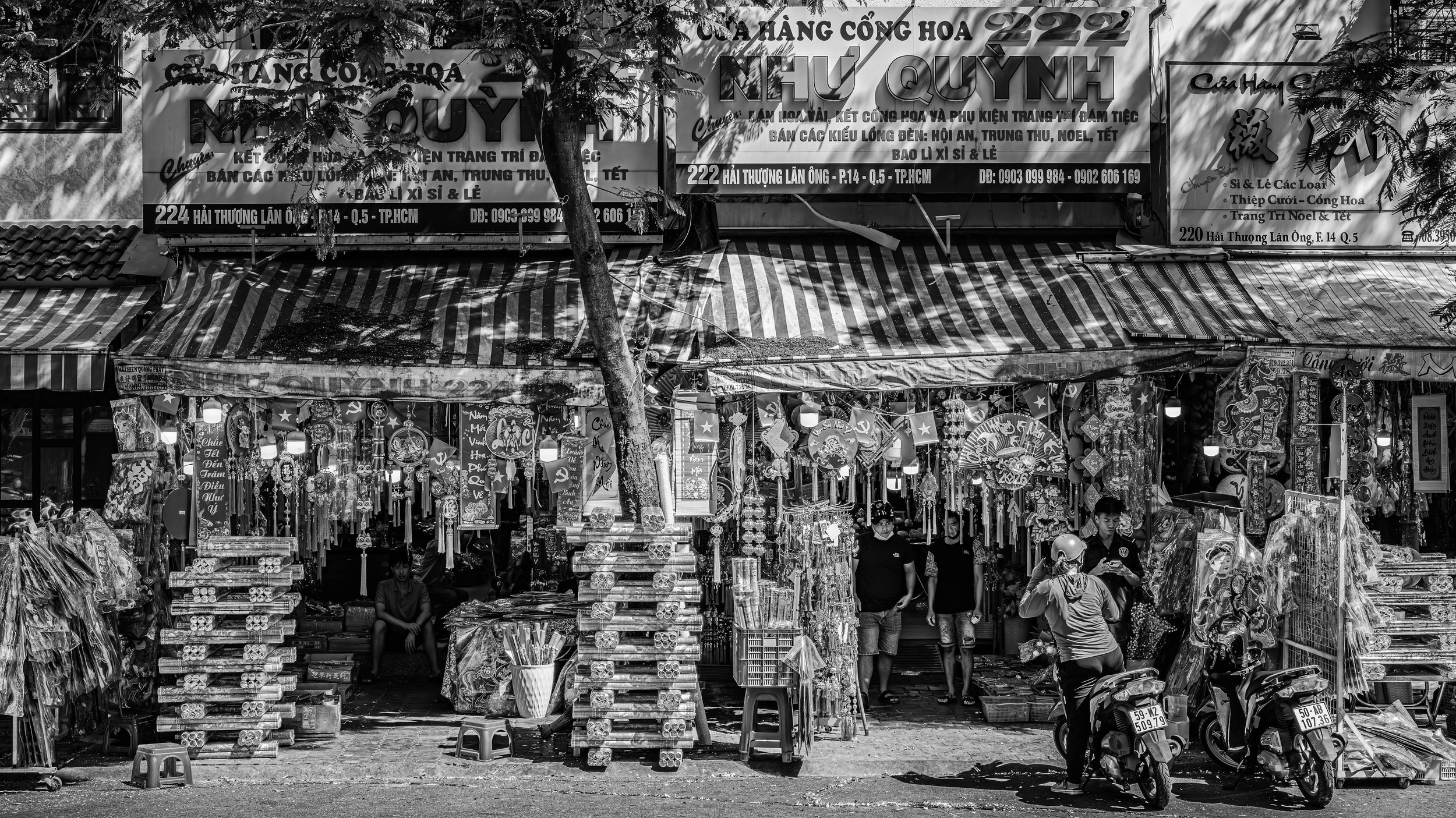 Street market stall selling colorful decorative items, lanterns, and souvenirs with signboards in Vietnamese above and people browsing.