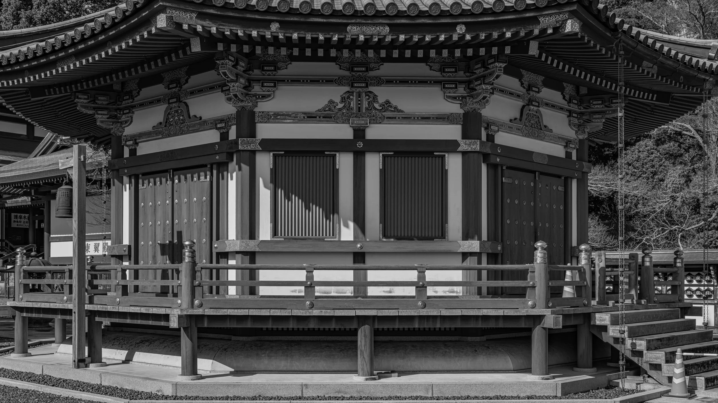Black and white photo of a traditional Japanese shrine building with intricate woodwork and a tiled roof, surrounded by a wooden fence.