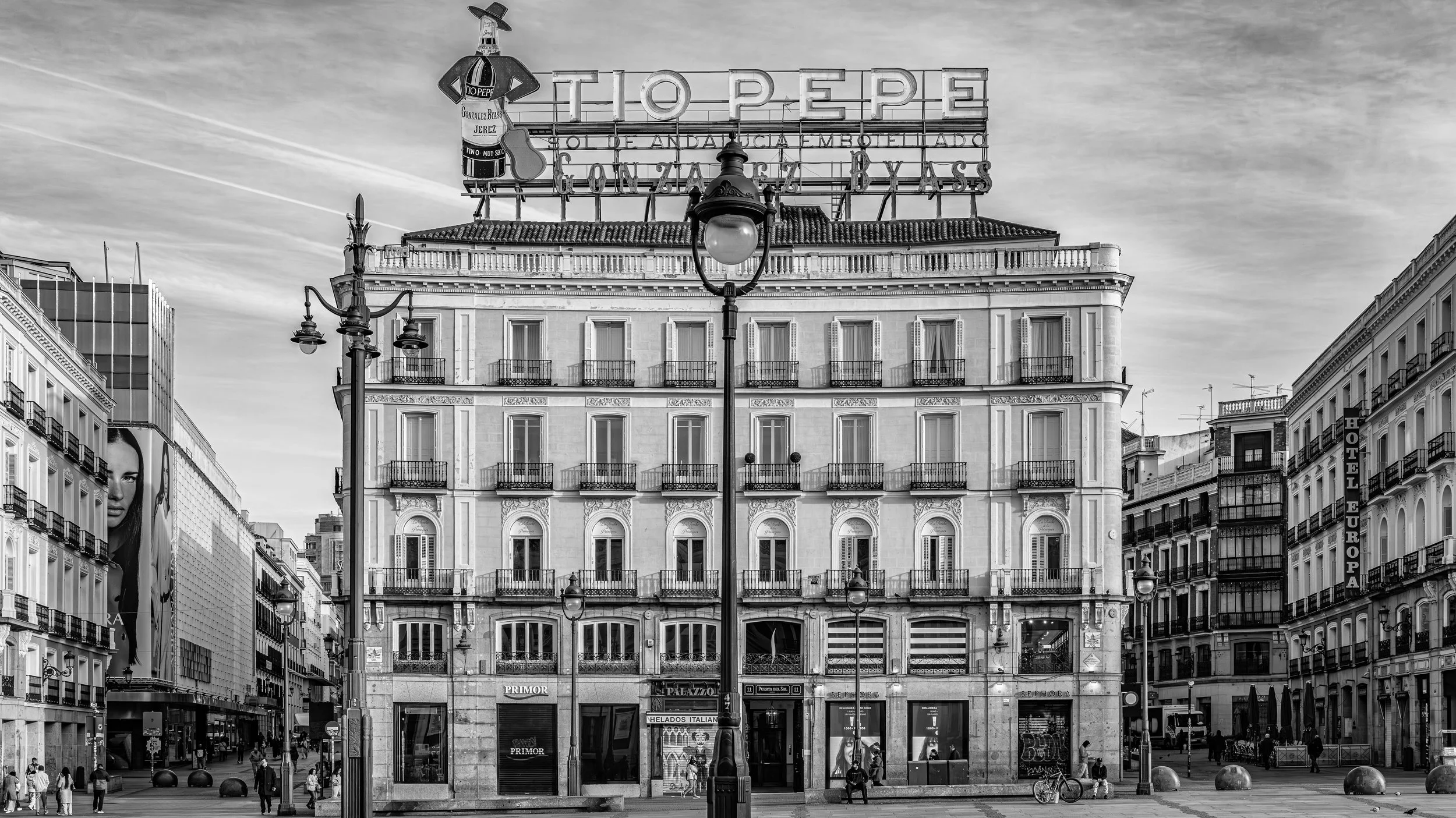 Black and white city street view showing a multi-story building with storefronts on the ground level, balconies on upper floors, and a large neon sign that reads 'TIO PEPE'.