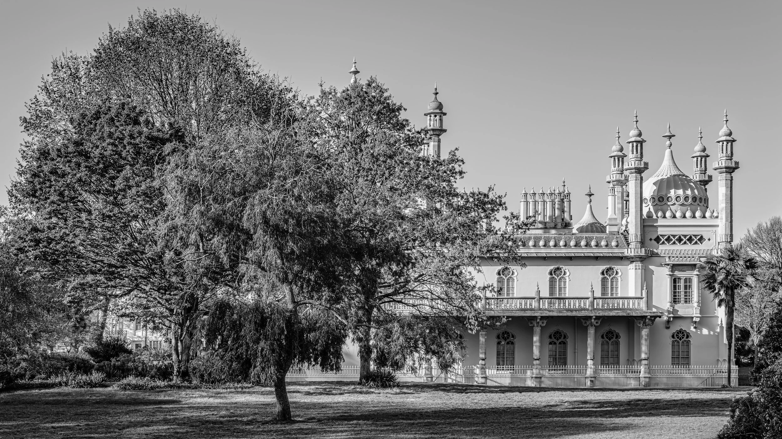 A large, ornate building with multiple towers and domes, surrounded by trees, in black and white.