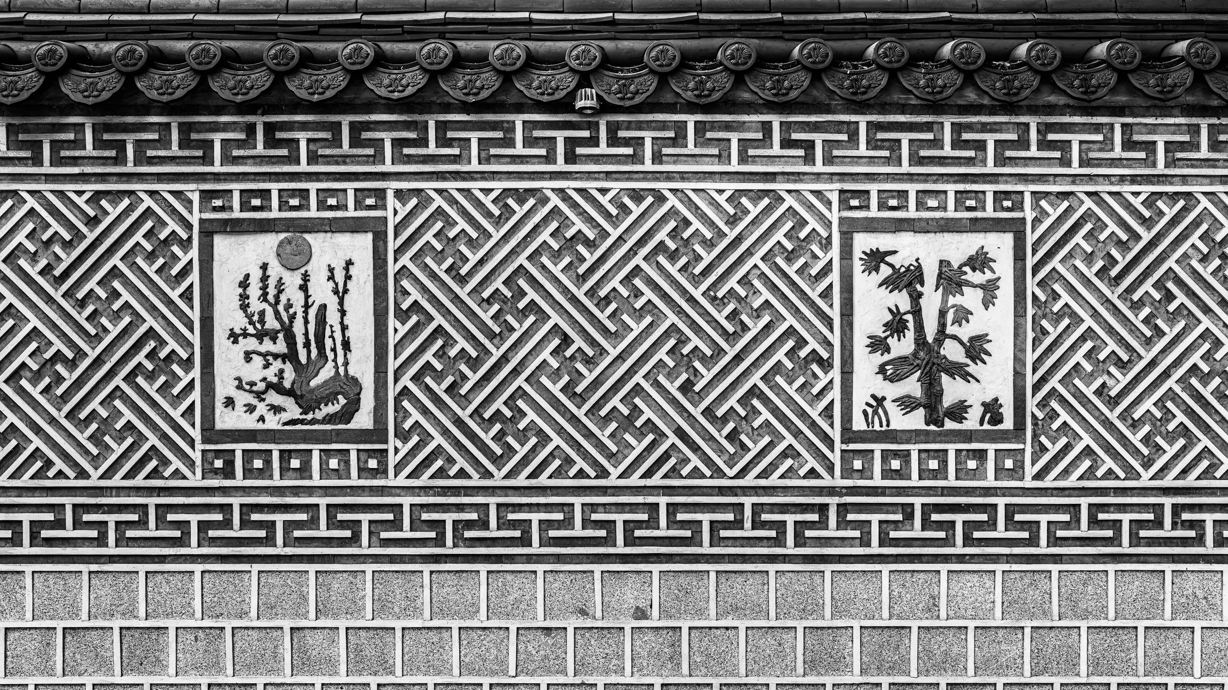 Black and white photograph of a decorative wall with intricate geometric patterns and two panels featuring stylized trees.