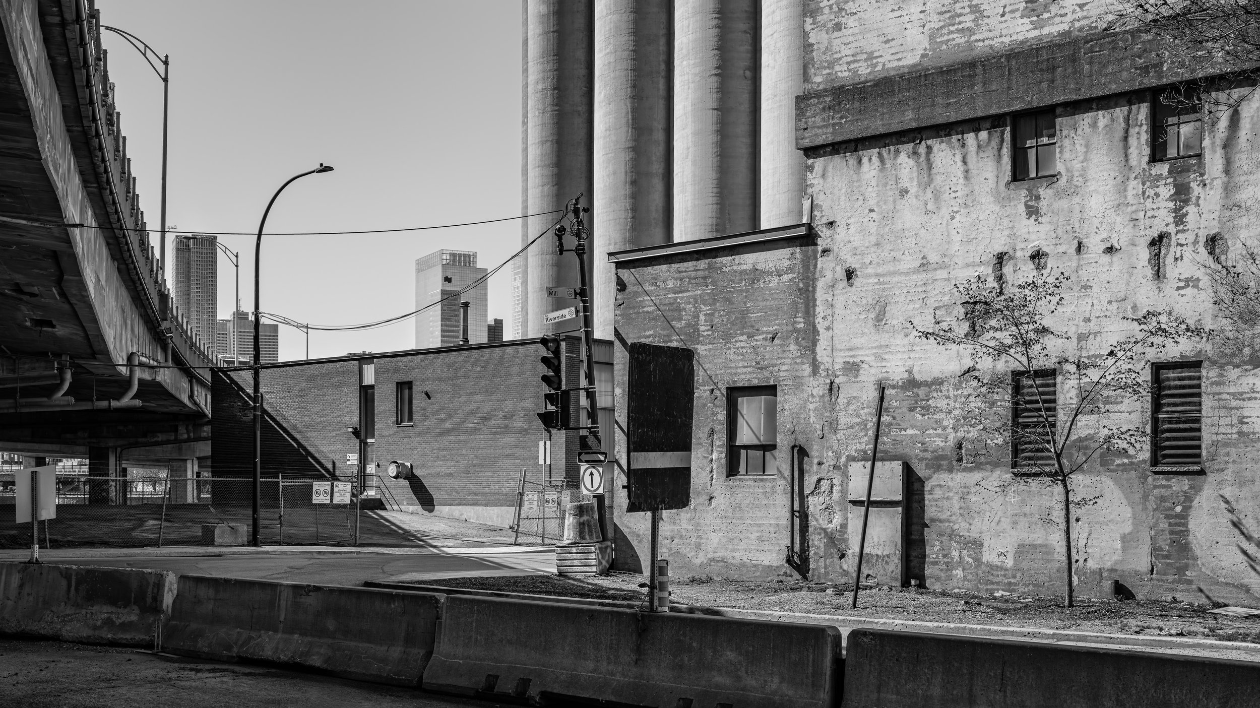 Black and white photo of an urban scene with old buildings, a street, utility poles, traffic lights, and modern skyscrapers in the background.