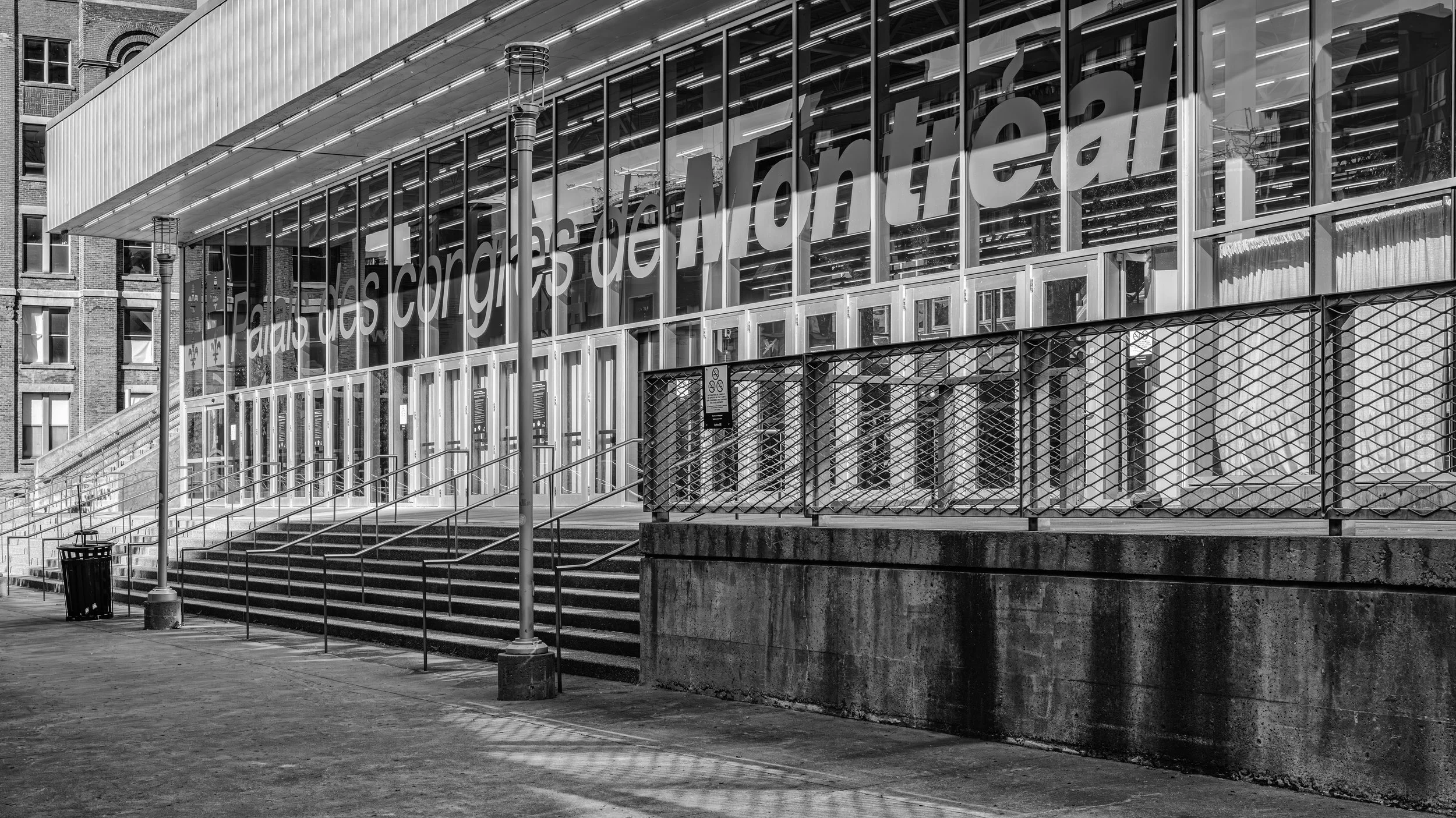Black and white photo of the front entrance of the New York Public Library with large glass windows and a sign saying 'Books are the gateway to knowledge' in French. There are stairs, street lamps, a trash can, and a gated area in front of the librar