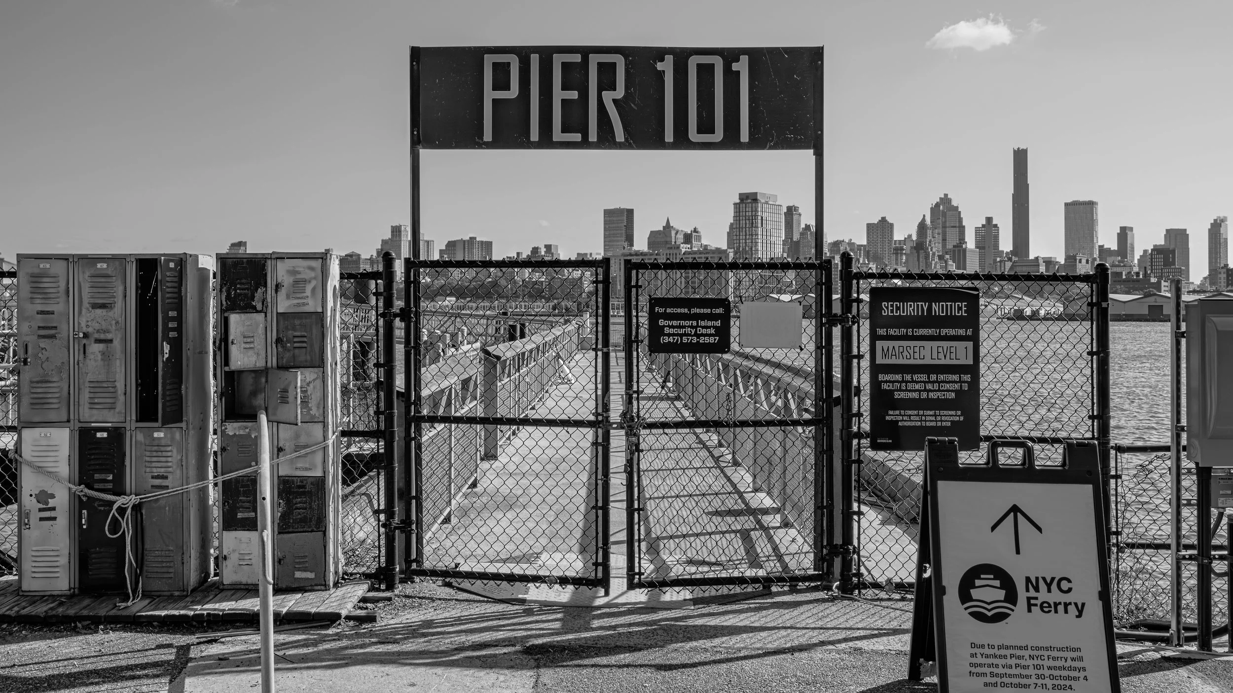 Closure gate at NYC Ferry with a city skyline in the background, including various tall buildings and a large sign that reads 'PER 101'. Governors Island, New York, USA.