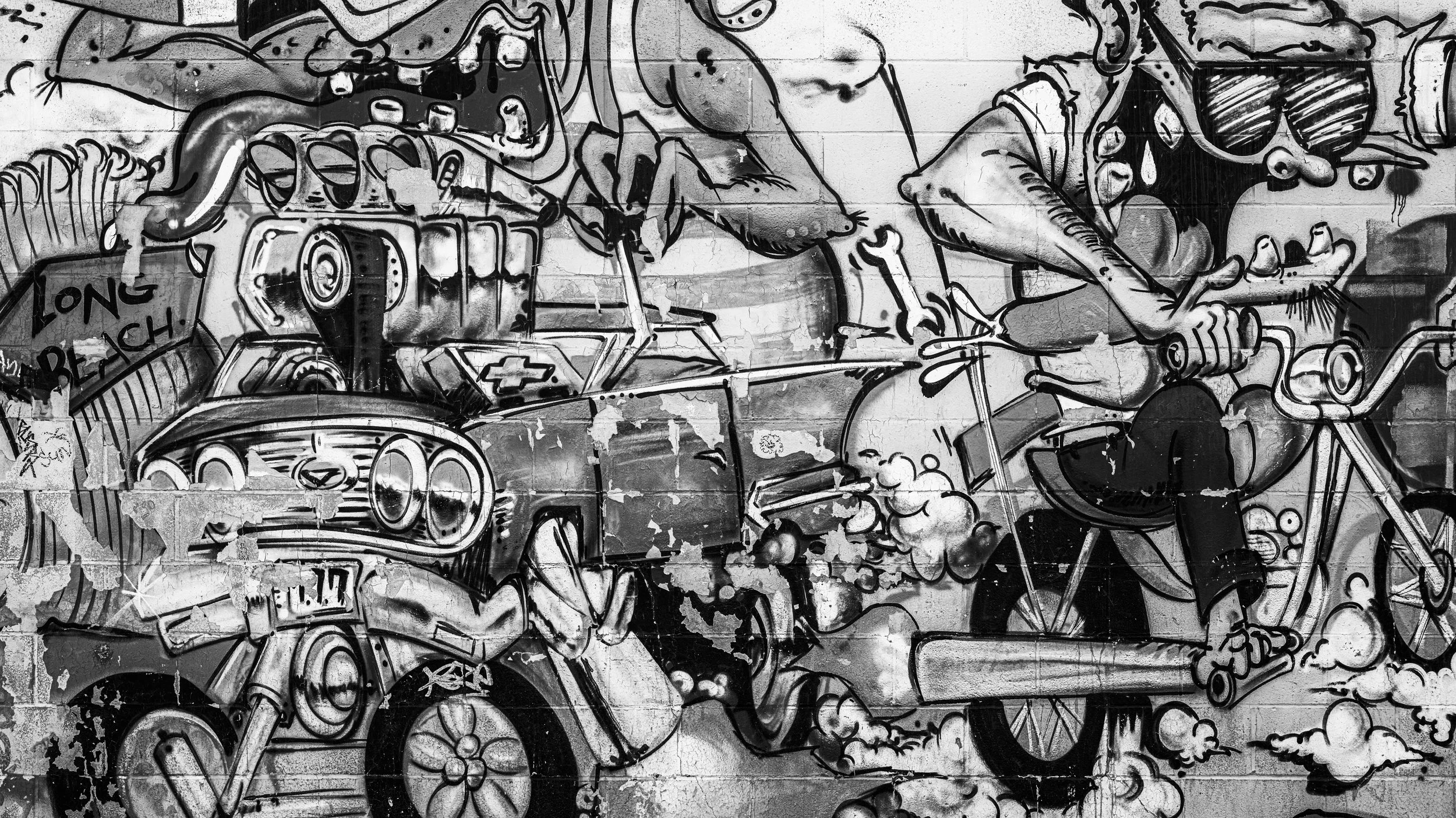 Black and white graffiti of a motorcycle and a person taking a selfie with a bicycle, on a brick wall.
